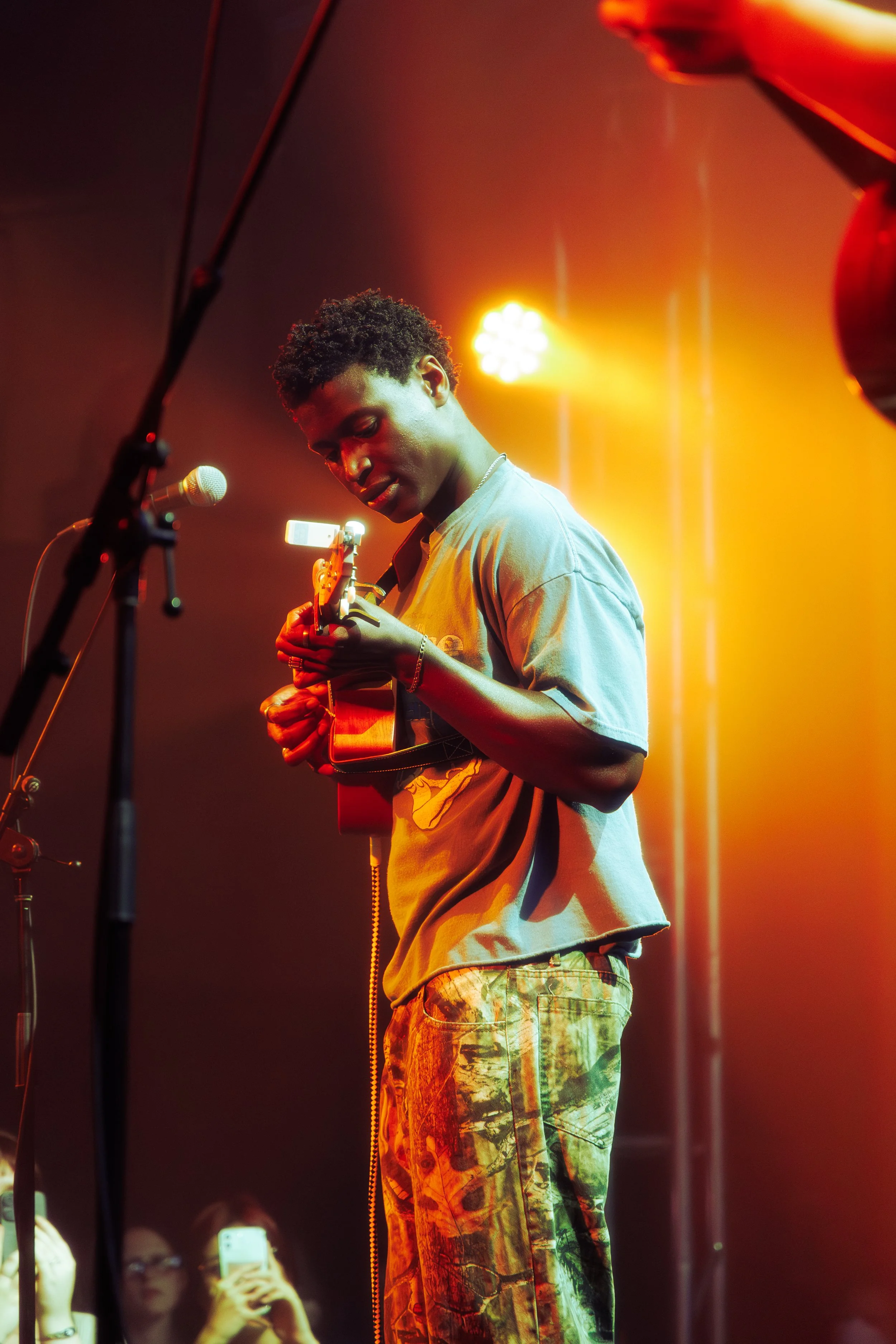 Young man playing an acoustic guitar on stage with yellow and orange stage lighting.