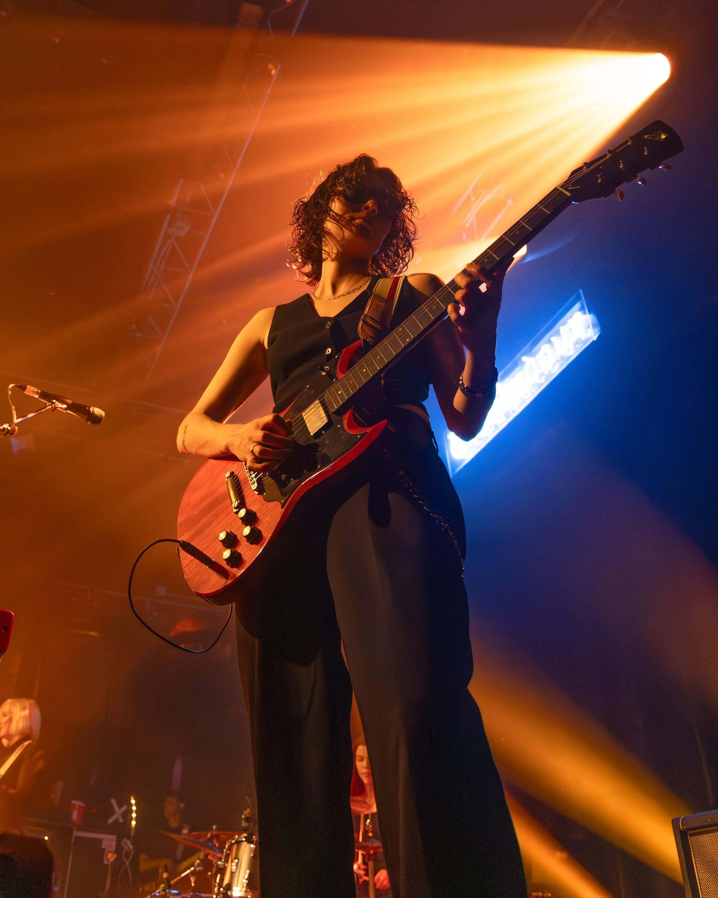 A woman playing an electric guitar on stage with colorful stage lighting.