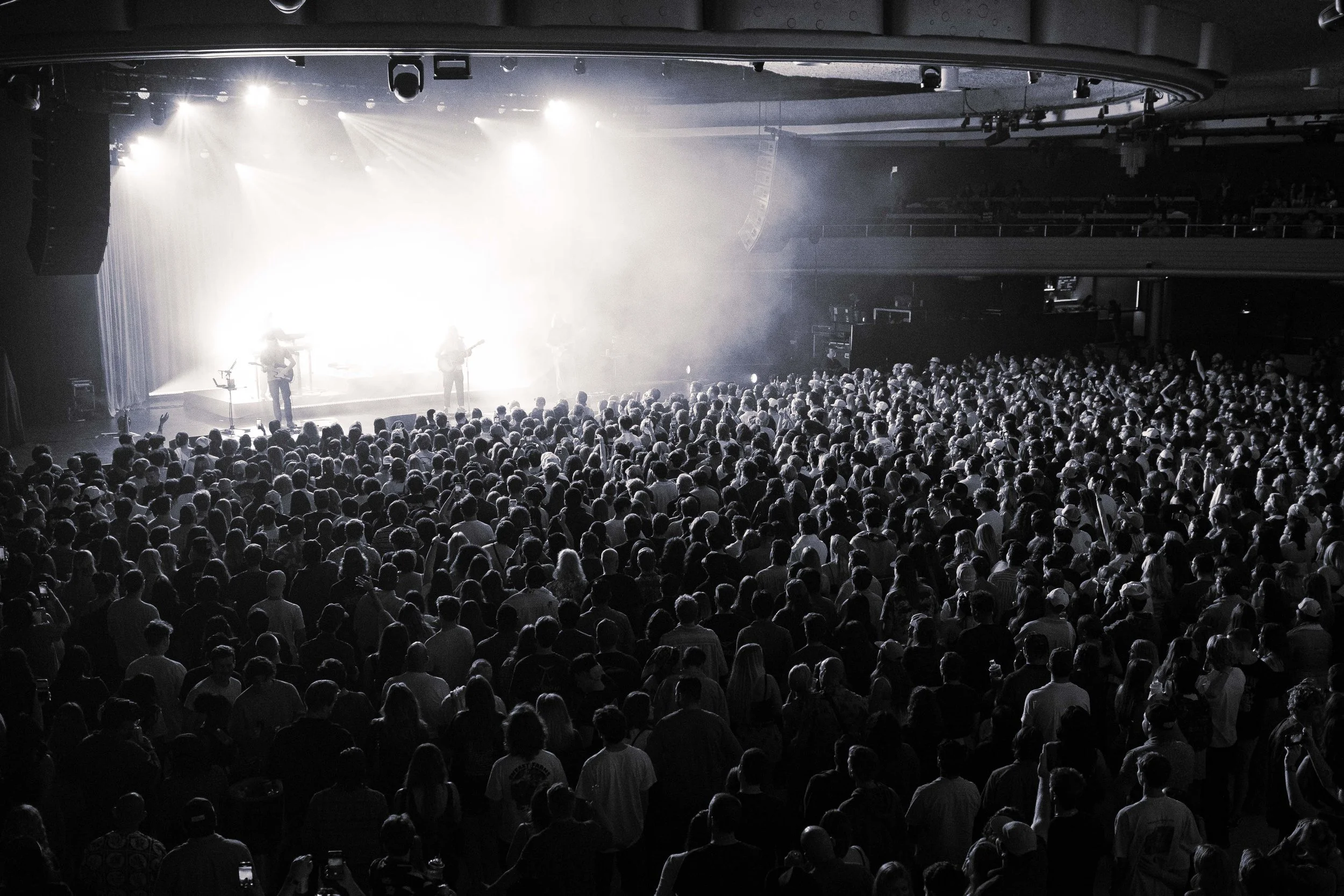 Black and white photo of a crowded concert with a stage in the background and band performing.