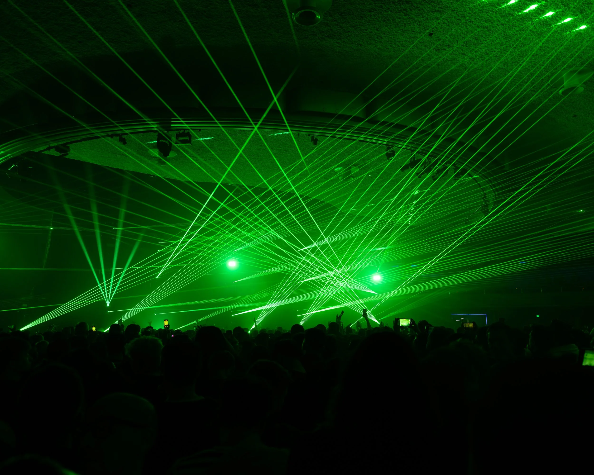 Green laser light show with a crowd of people watching in an indoor venue.