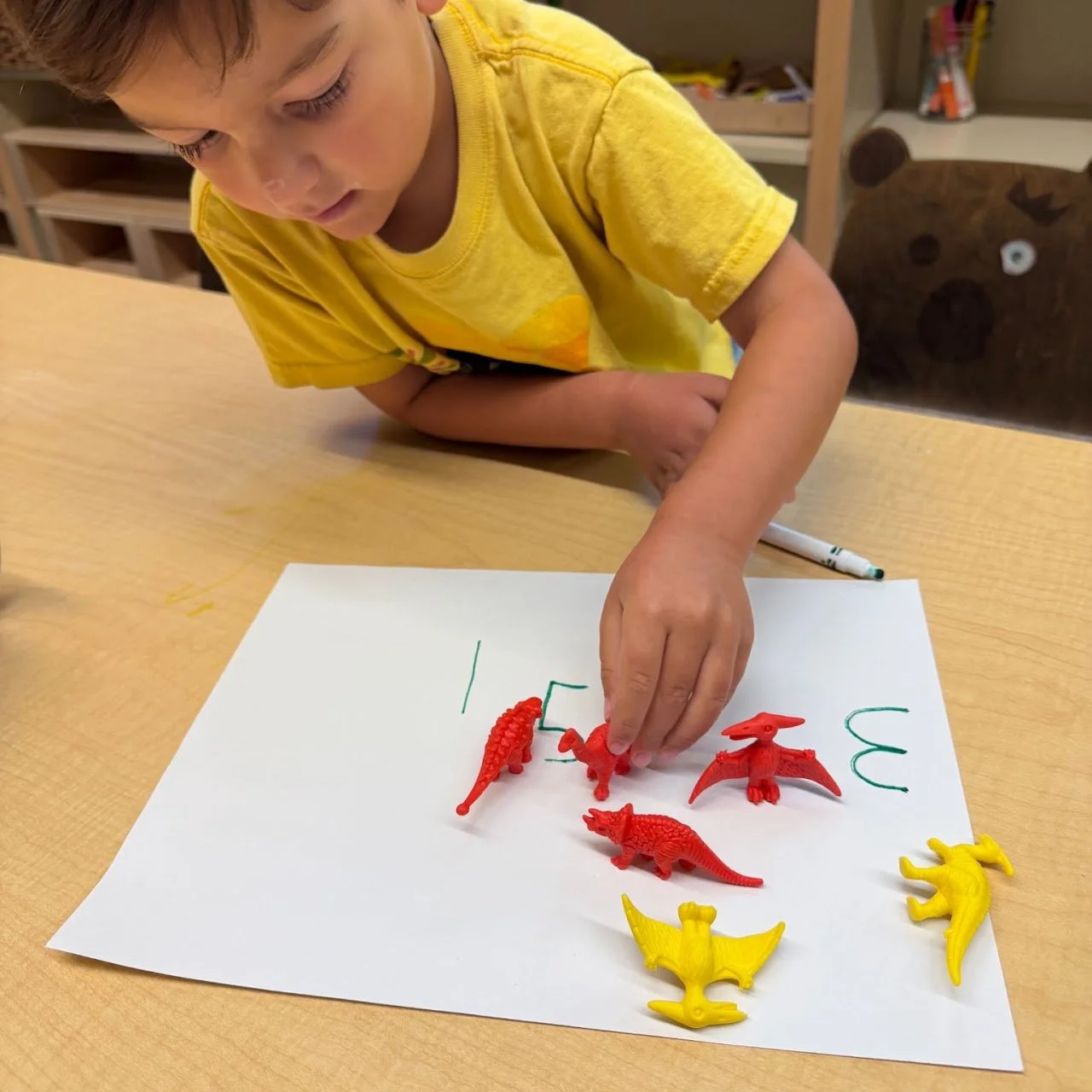 Boy playing with toy dinosaurs on a piece of paper with numbers