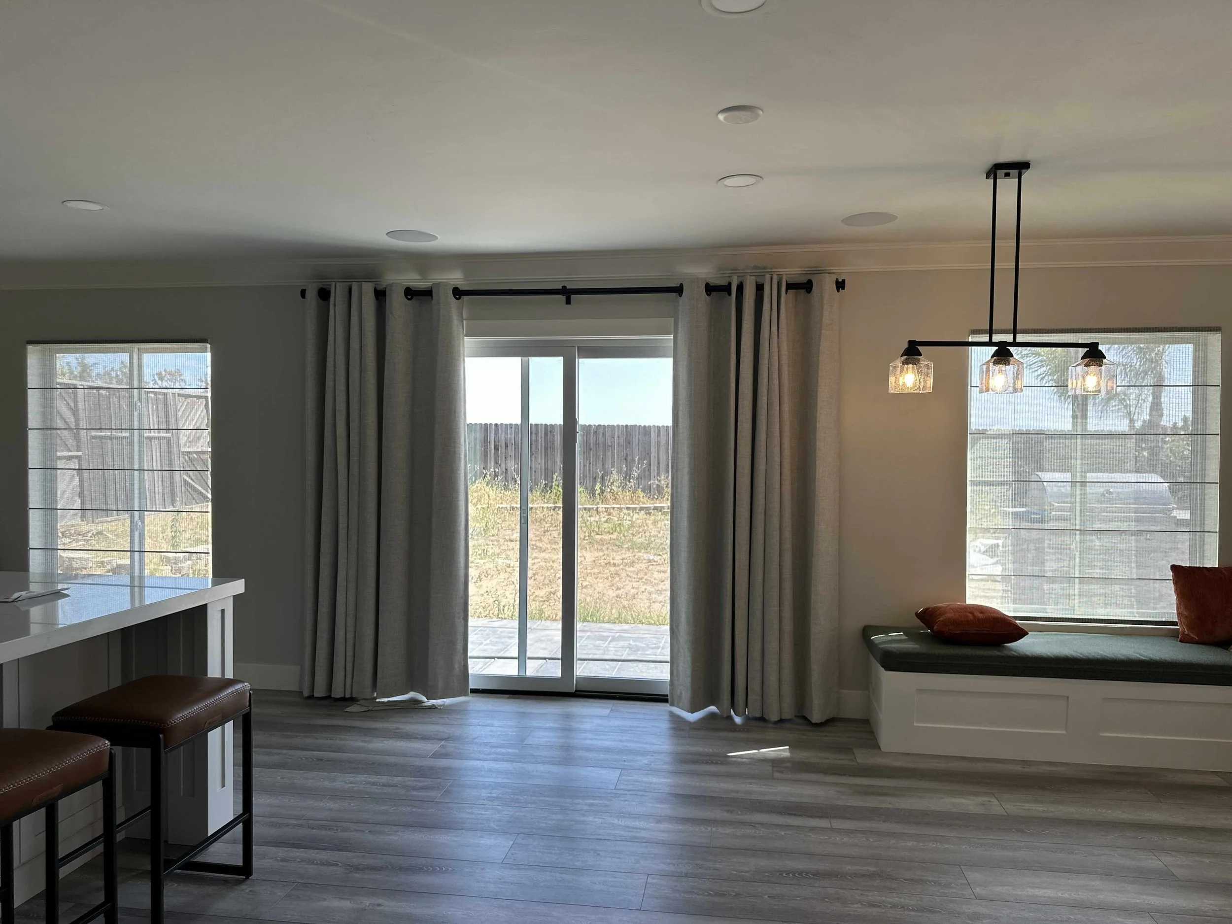 Living room with a pair of roman shades framing a glass sliding door with curtains.