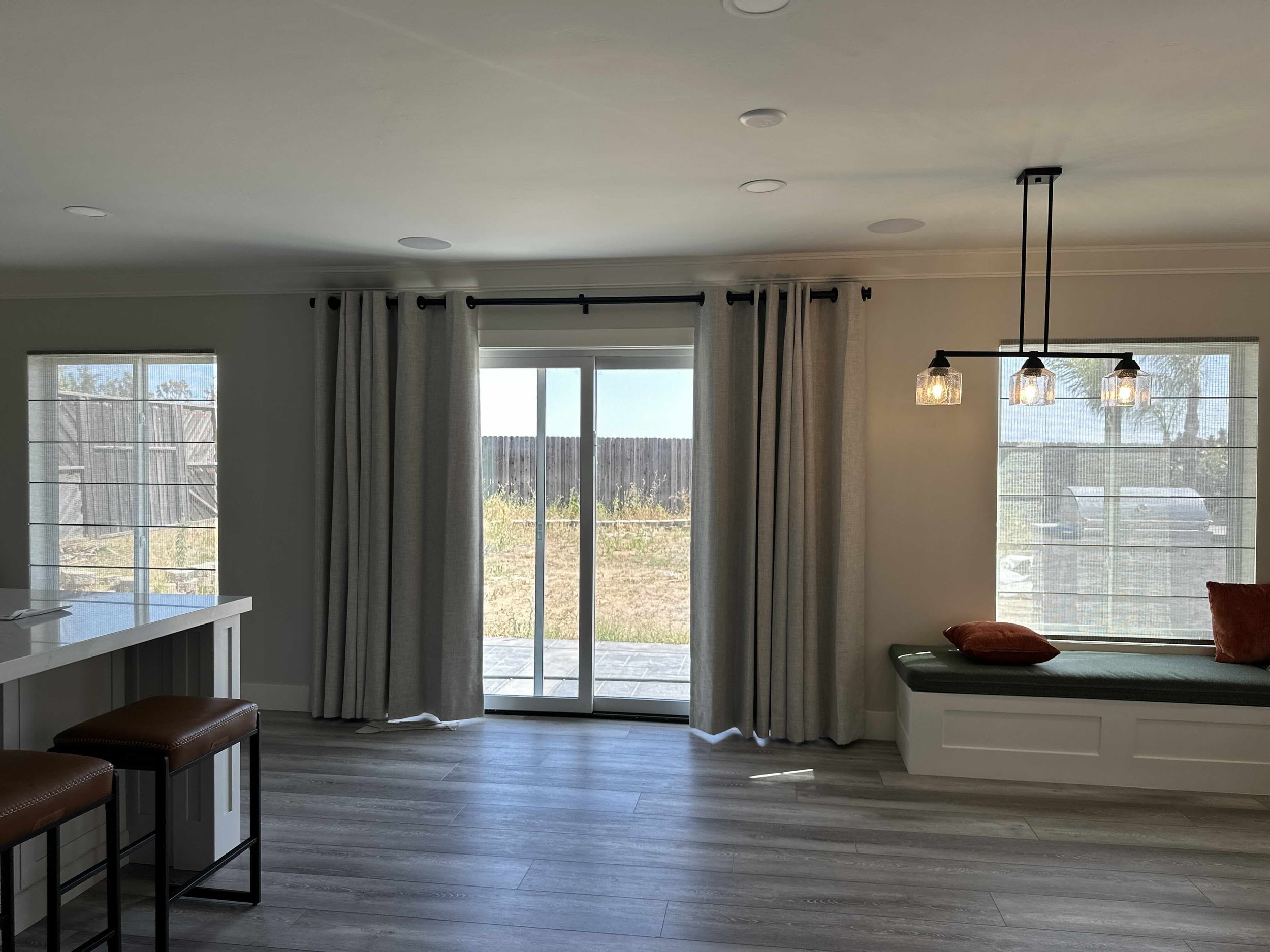 Living room with sliding glass doors, white curtains, pendant lights, seating area with red pillows, and a window with blinds.