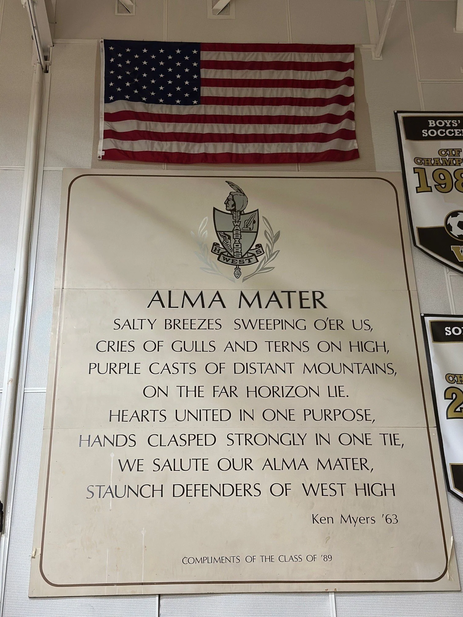 American flag hanging above a school crest and a poem on a school poster.