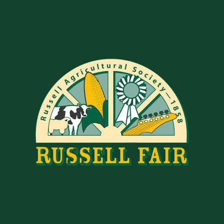 The logo of the Russell Fair, featuring images of a cow, a calf, a corn ear, a ribbon award, and a boat, with a green background and yellow text.