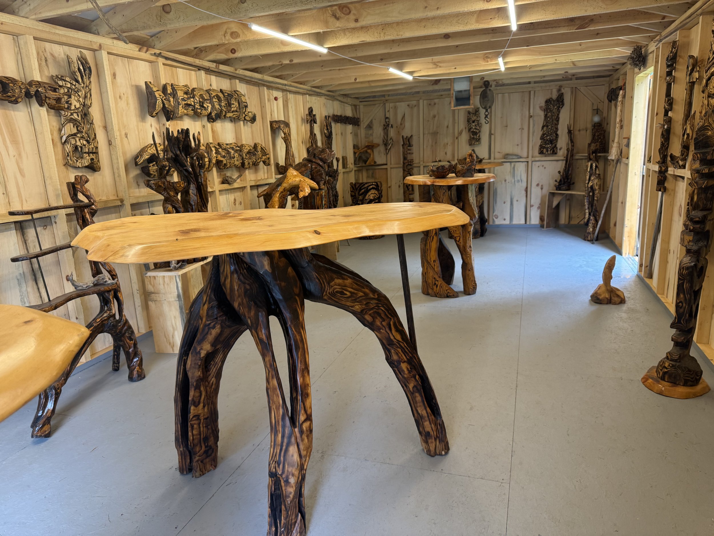 A room displaying wooden furniture and wall art made from carved and polished wood, including chairs, tables, sculptures, and wall hangings in a rustic style.
