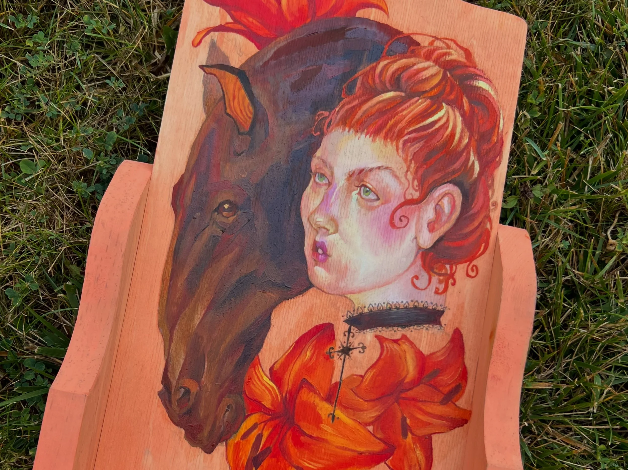 An illustration on a wooden board depicting a young girl with curly red hair, green eyes, and light skin, alongside a black and brown dog with pointed ears, set against orange and red background flames.