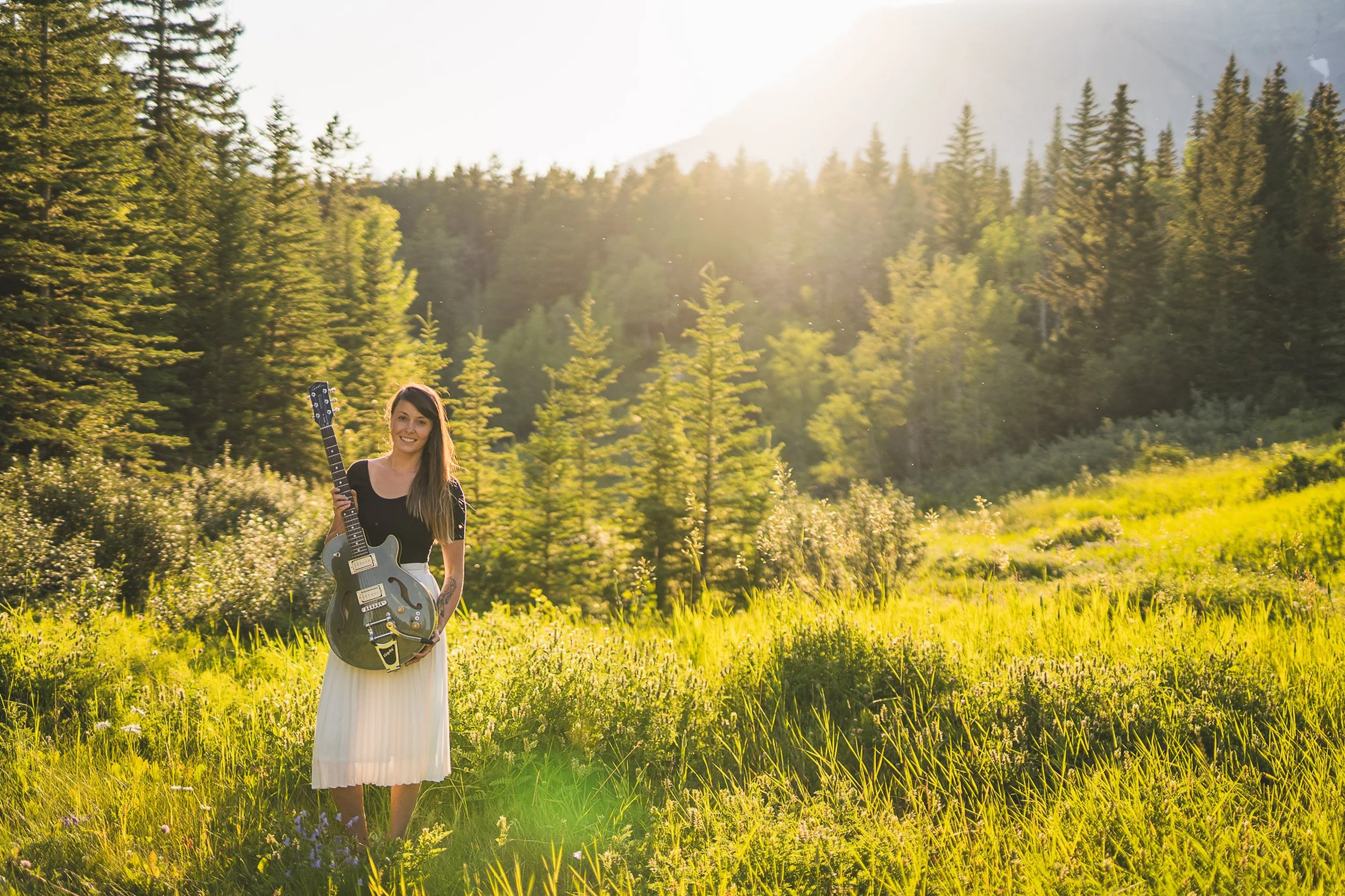 Musician Alanna J Brown standing in a sunlit grassy field.