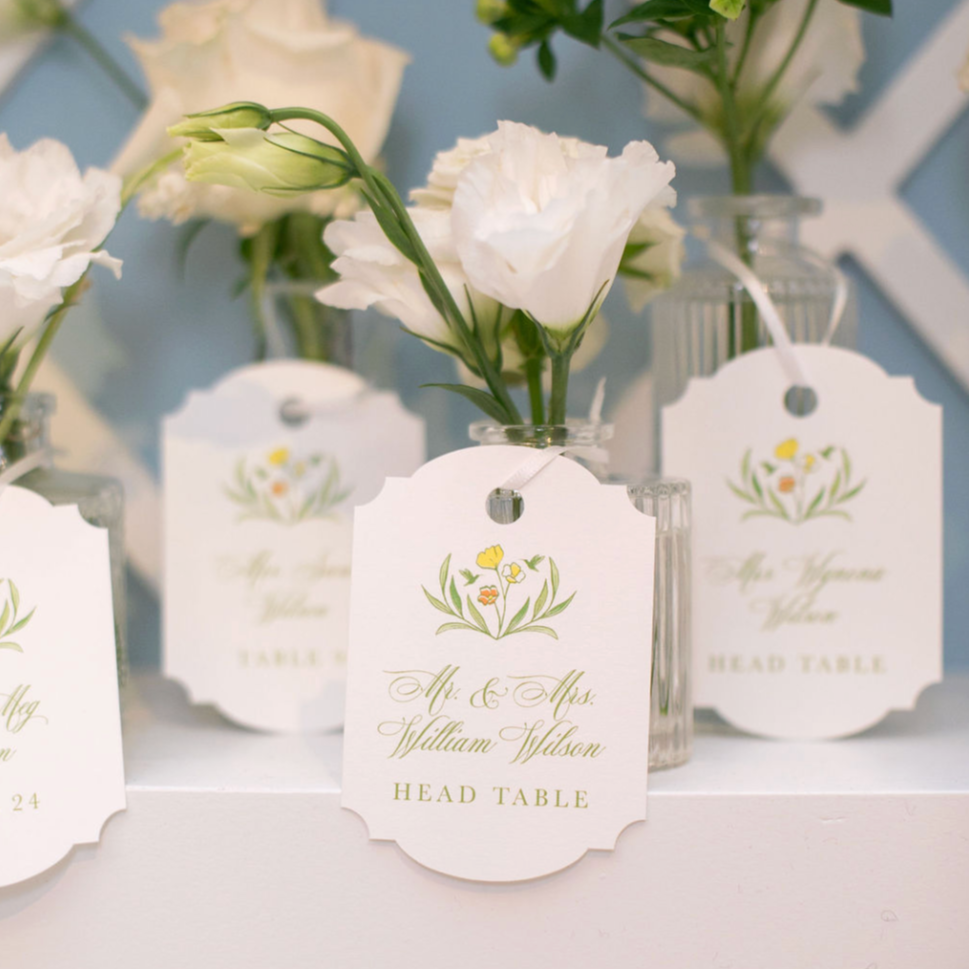 Wedding seating cards with white flowers in glass vases on a table.