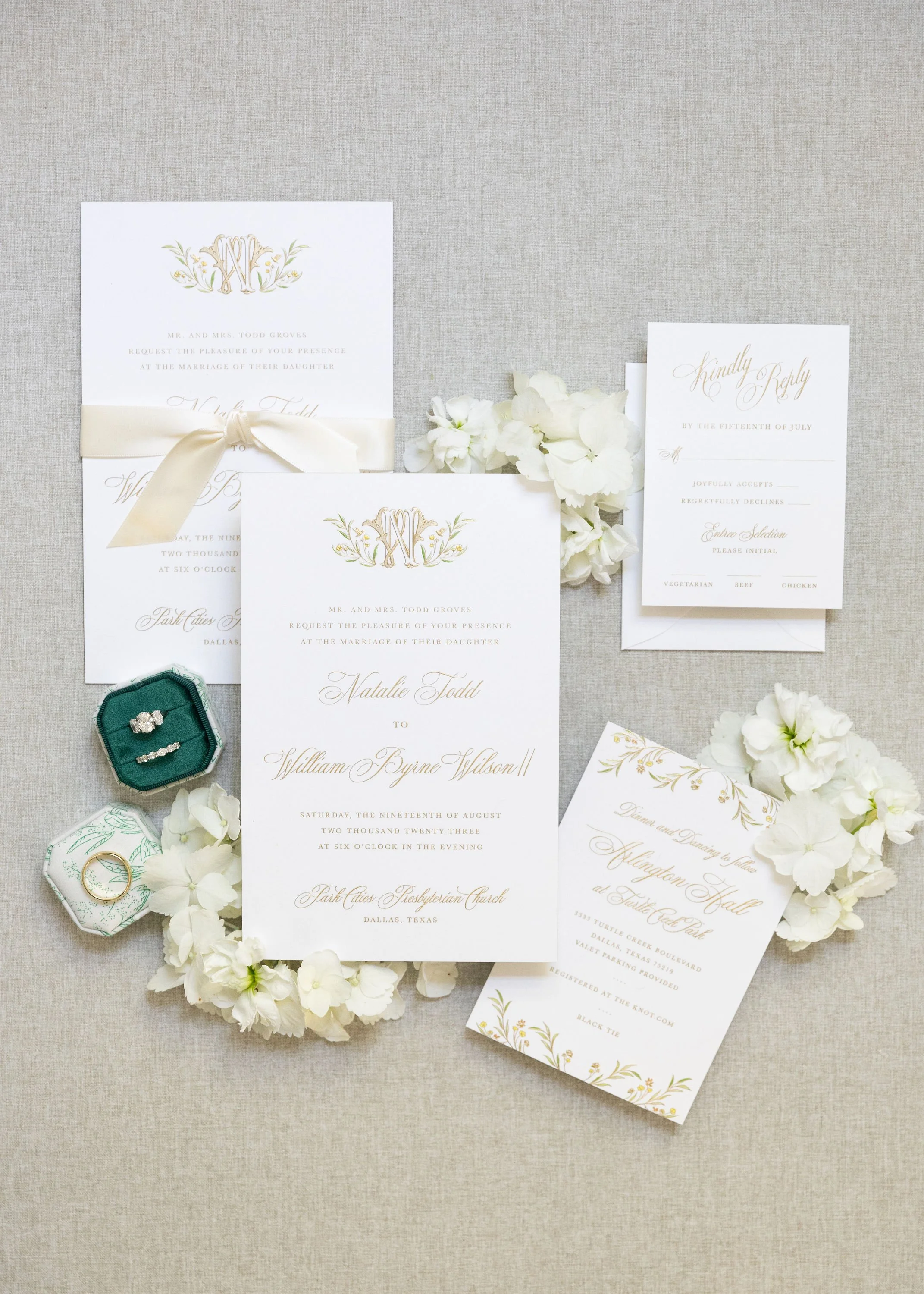 Wedding invitation suite with floral accents, rings in green velvet and white fabric boxes, and RSVP cards on a beige background.