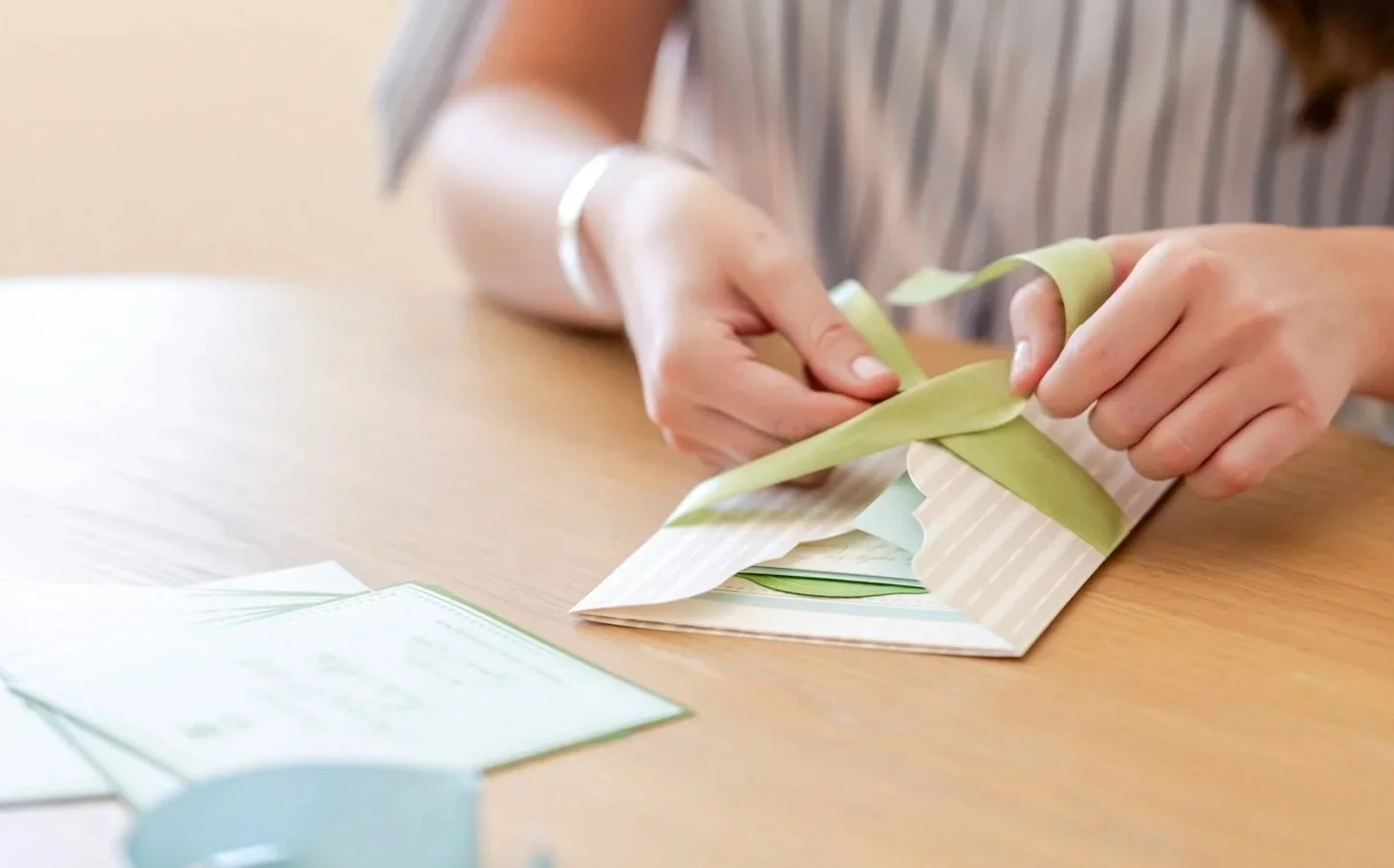 Person wrapping a gift with green and striped wrapping paper on a wooden table.