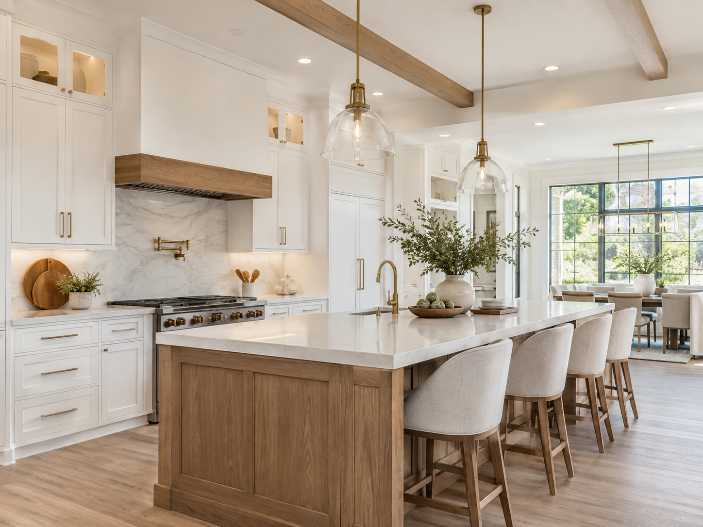 Bright, modern kitchen with white cabinetry, marble backsplash, wooden accents, large kitchen island with beige upholstered chairs, greenery in vases, and ample natural light from large windows in the dining area.