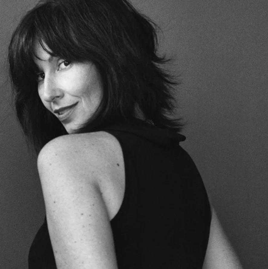 Black and white photo of Human Design reader Fiona Lindberg with shoulder-length, wavy hair looking over her shoulder and smiling.
