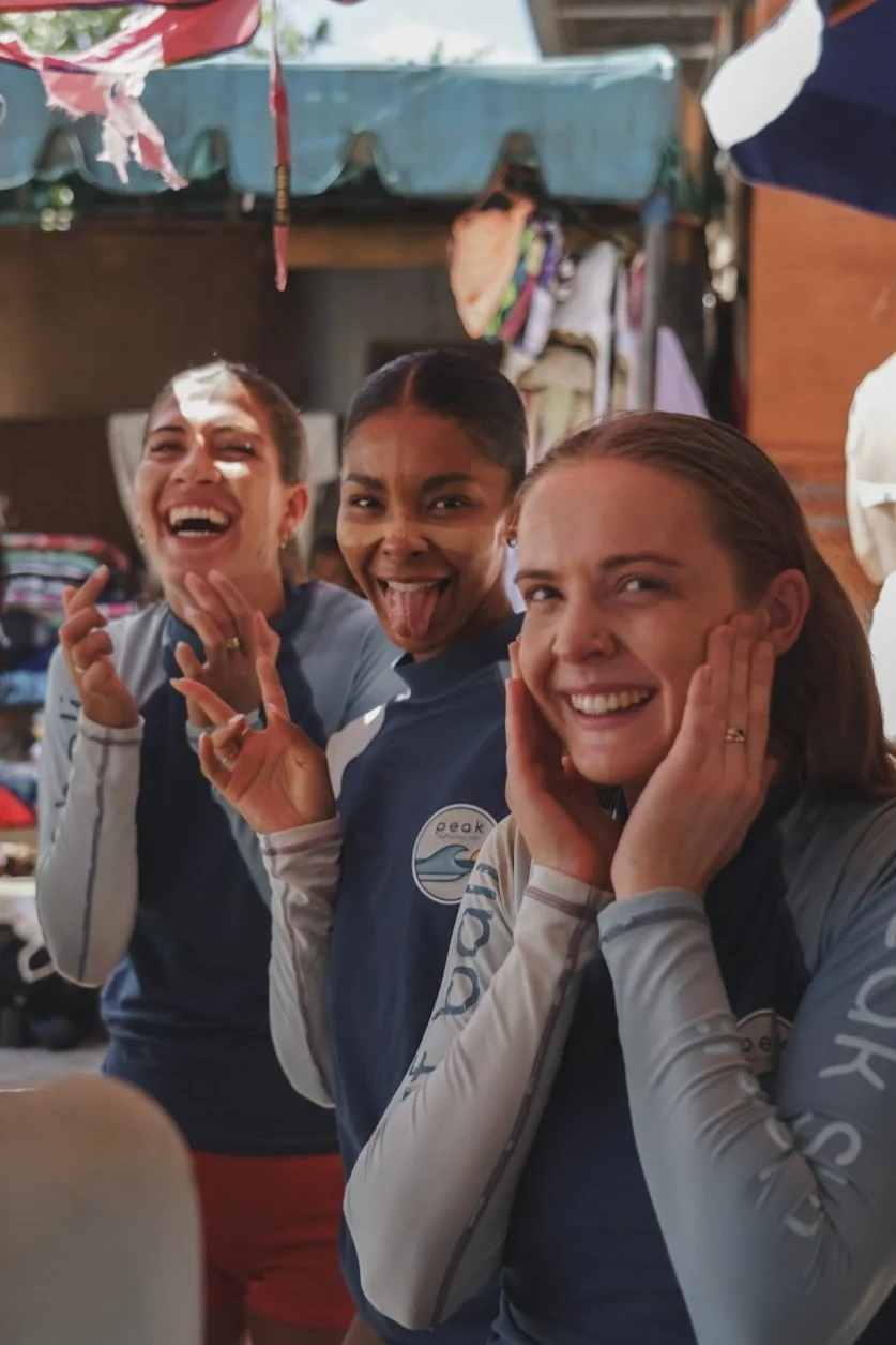 Peak Surf Bali Students at Padang Padang Beach Uluwatu  Yoga Retreat Yoga with Jordan Surfing Peak Surf Bali Surf School high five smiles fun happy joy friendship surfing beautiful beach crystal clear water white sand putting Zinc on face 