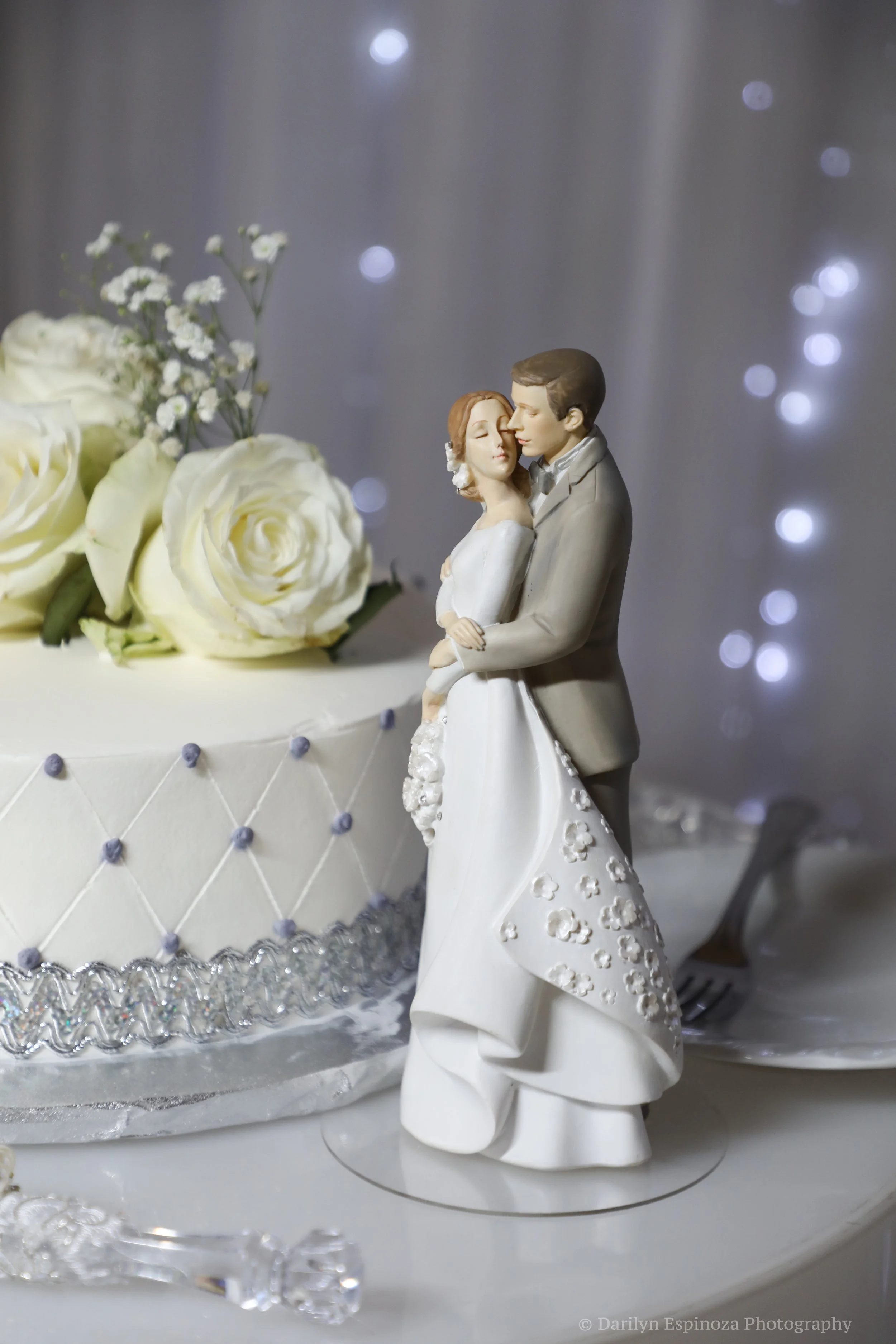 Wedding cake with white roses and a figurine of a bride and groom.