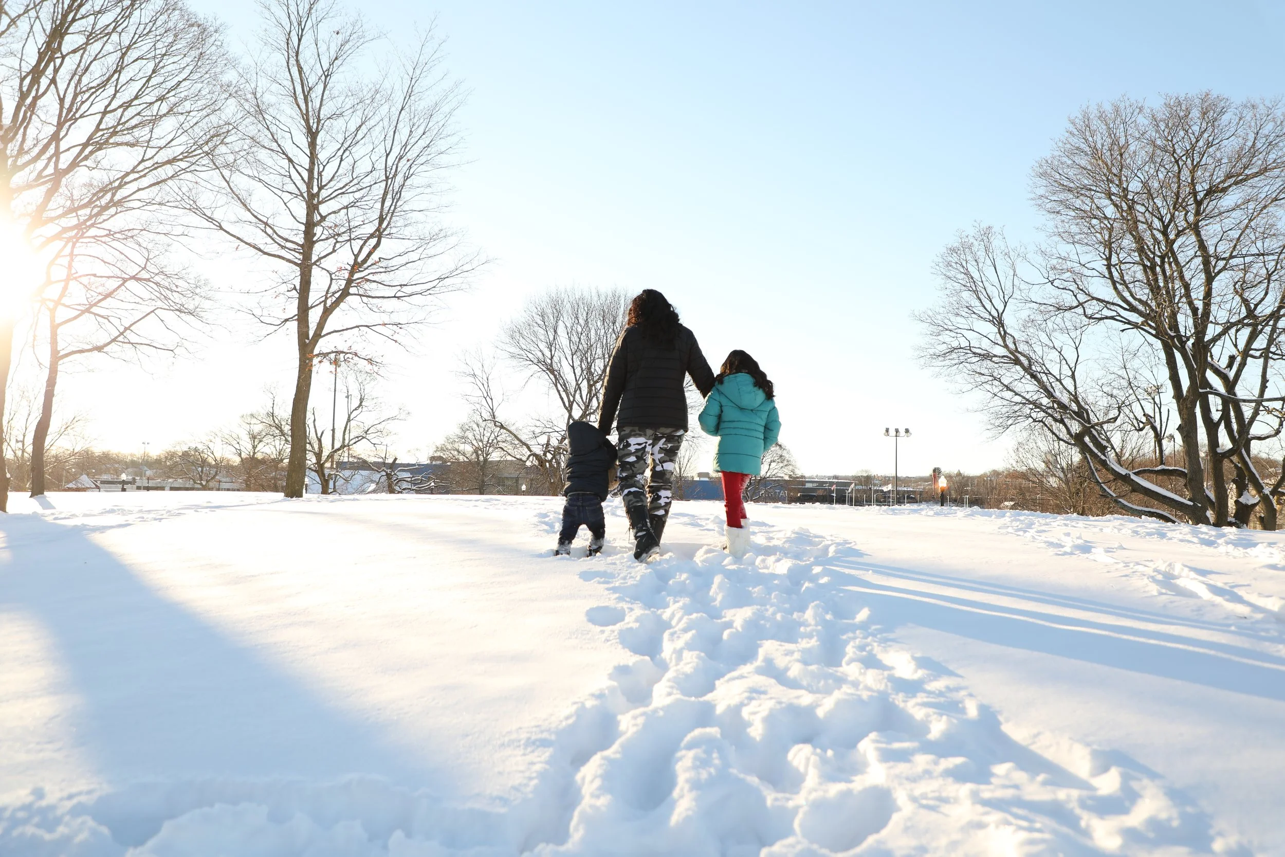Family walking through snowy park on winter day with leafless trees and a clear blue sky