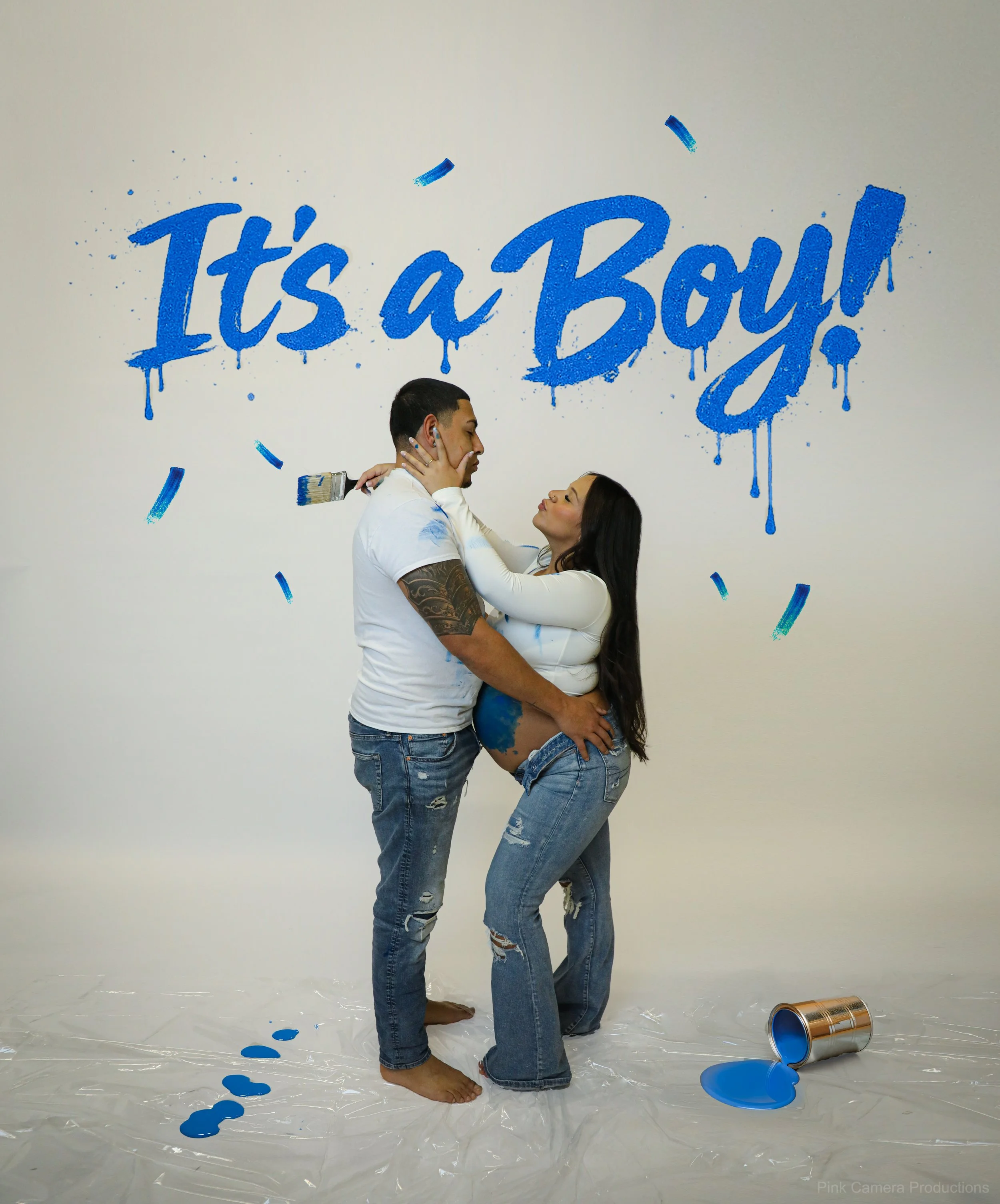Couple celebrating pregnancy with paint, 'It's a Boy!' mural, open paint can, and paint on floor.