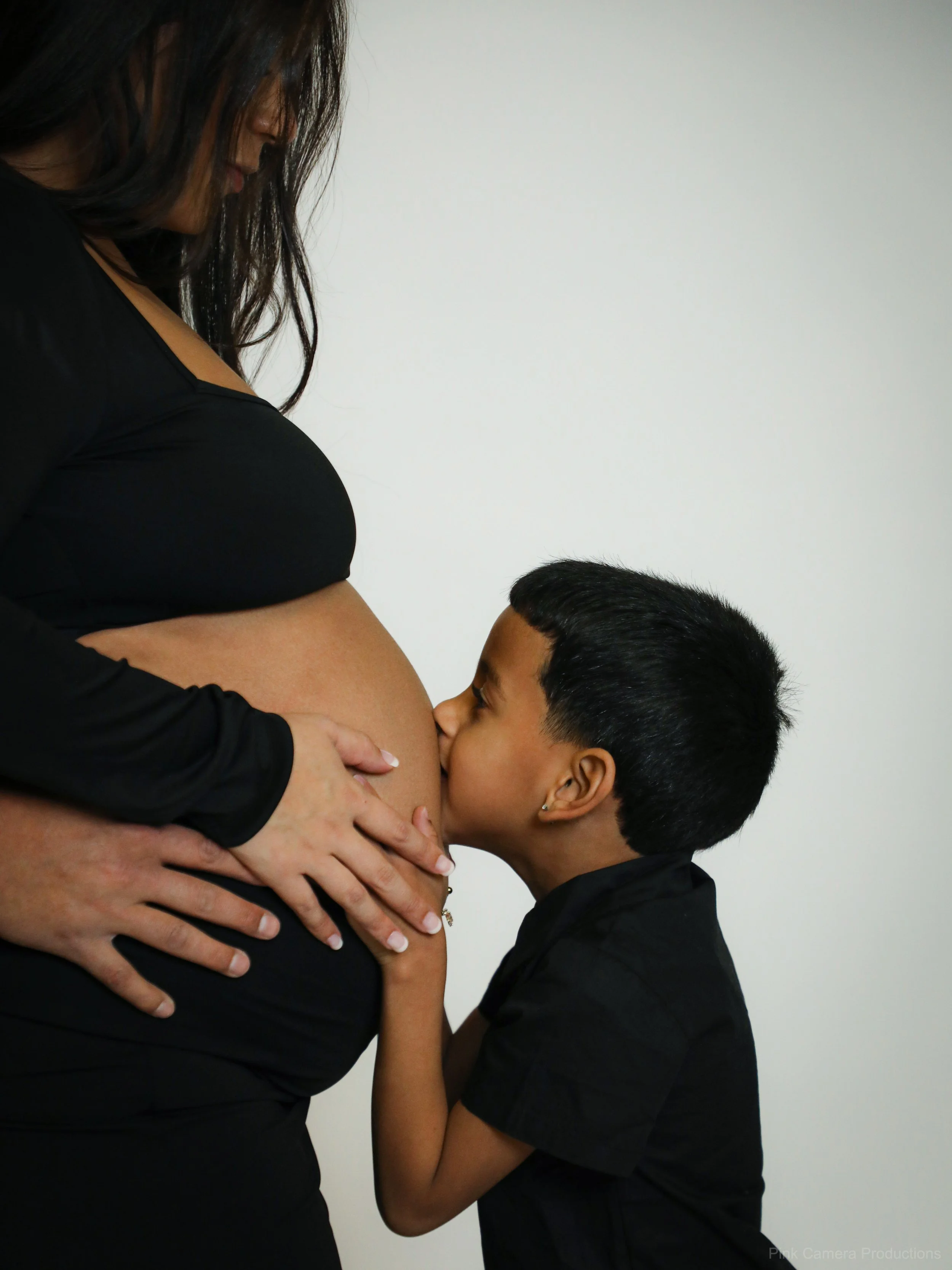 A young boy kissing a pregnant woman's belly.
