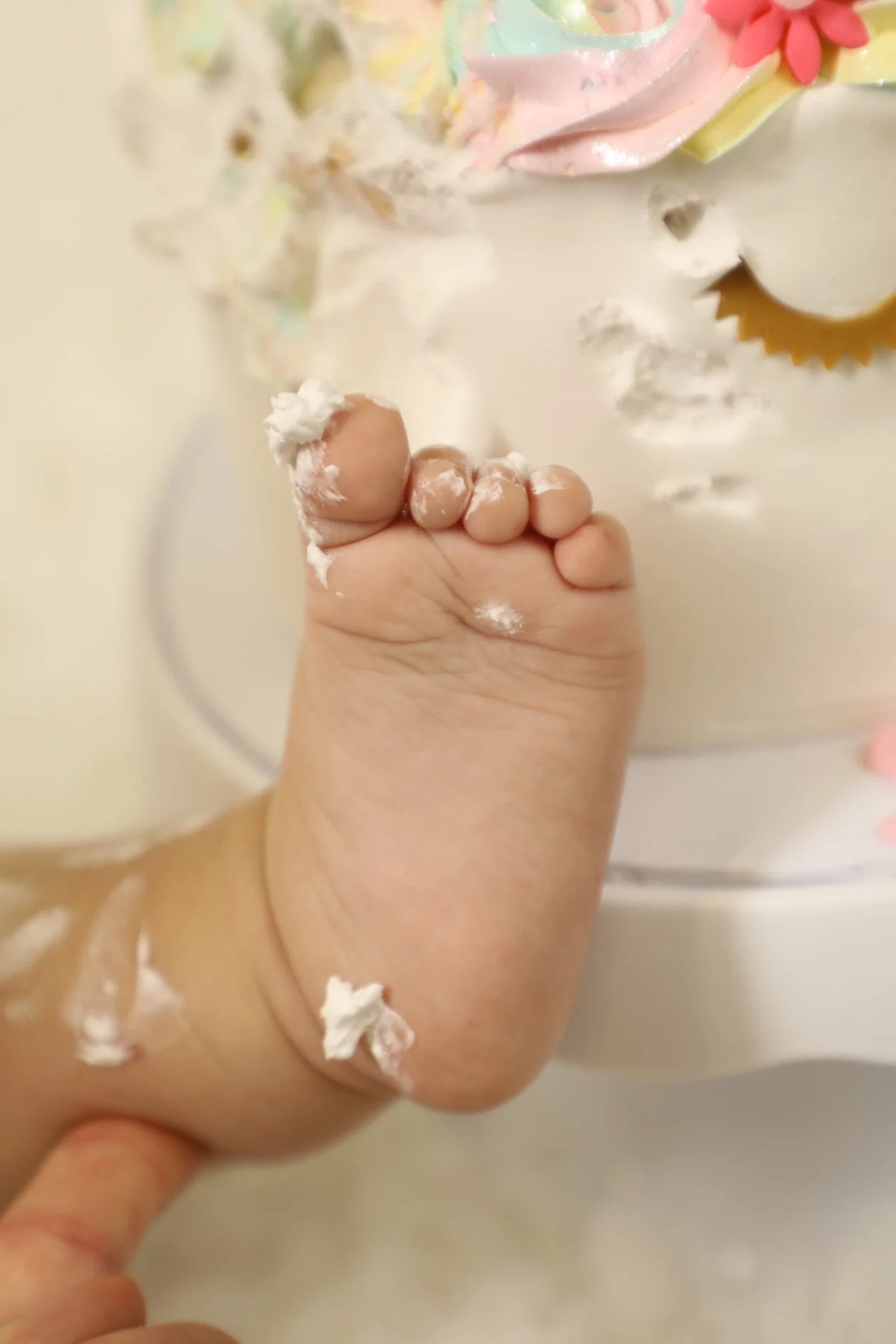 A child's foot with cream and frosting on it near a birthday cake with colorful icing and decorations.
