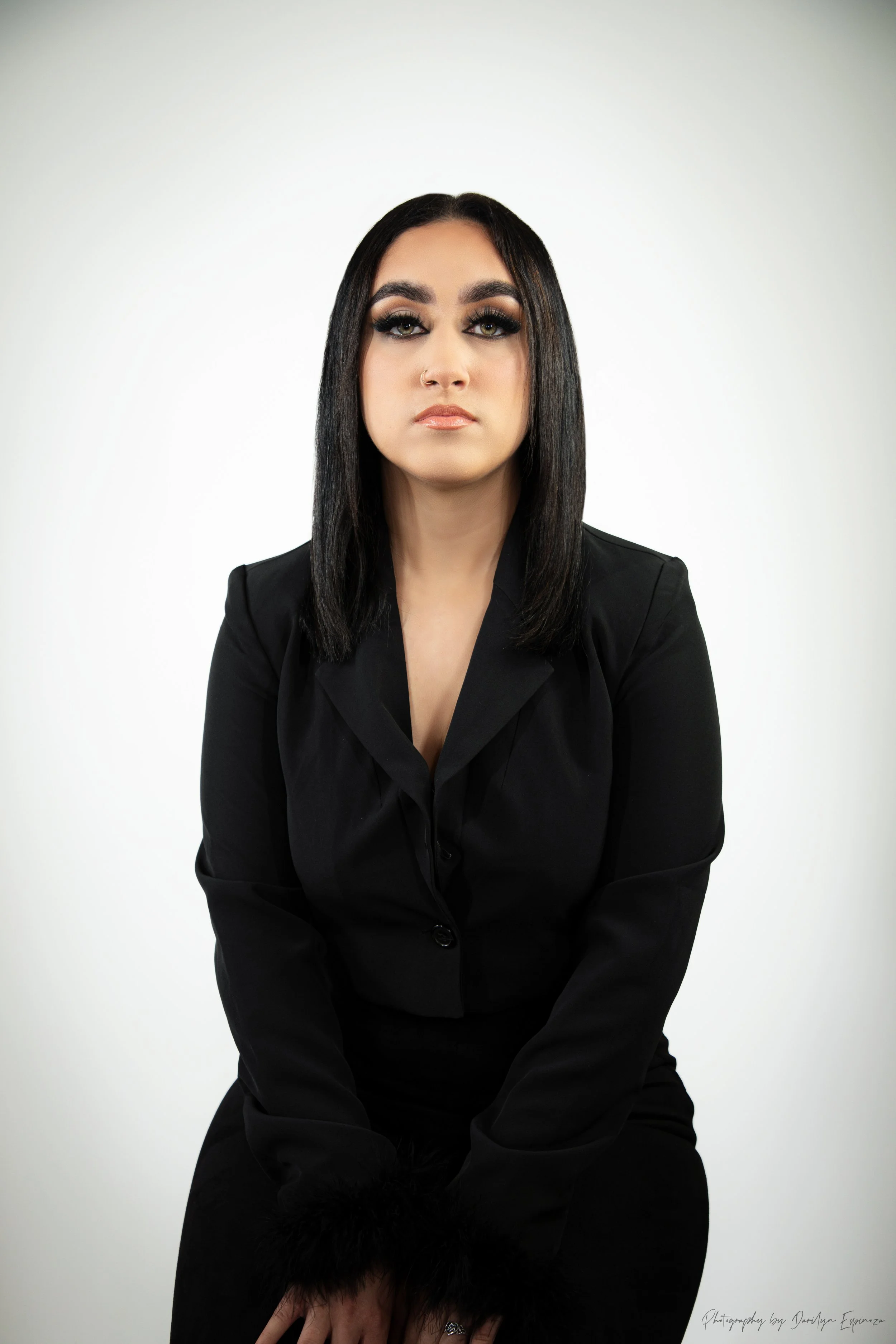 Portrait of a woman with straight dark hair, wearing a black blazer with fur cuff details, sitting against a plain white background.