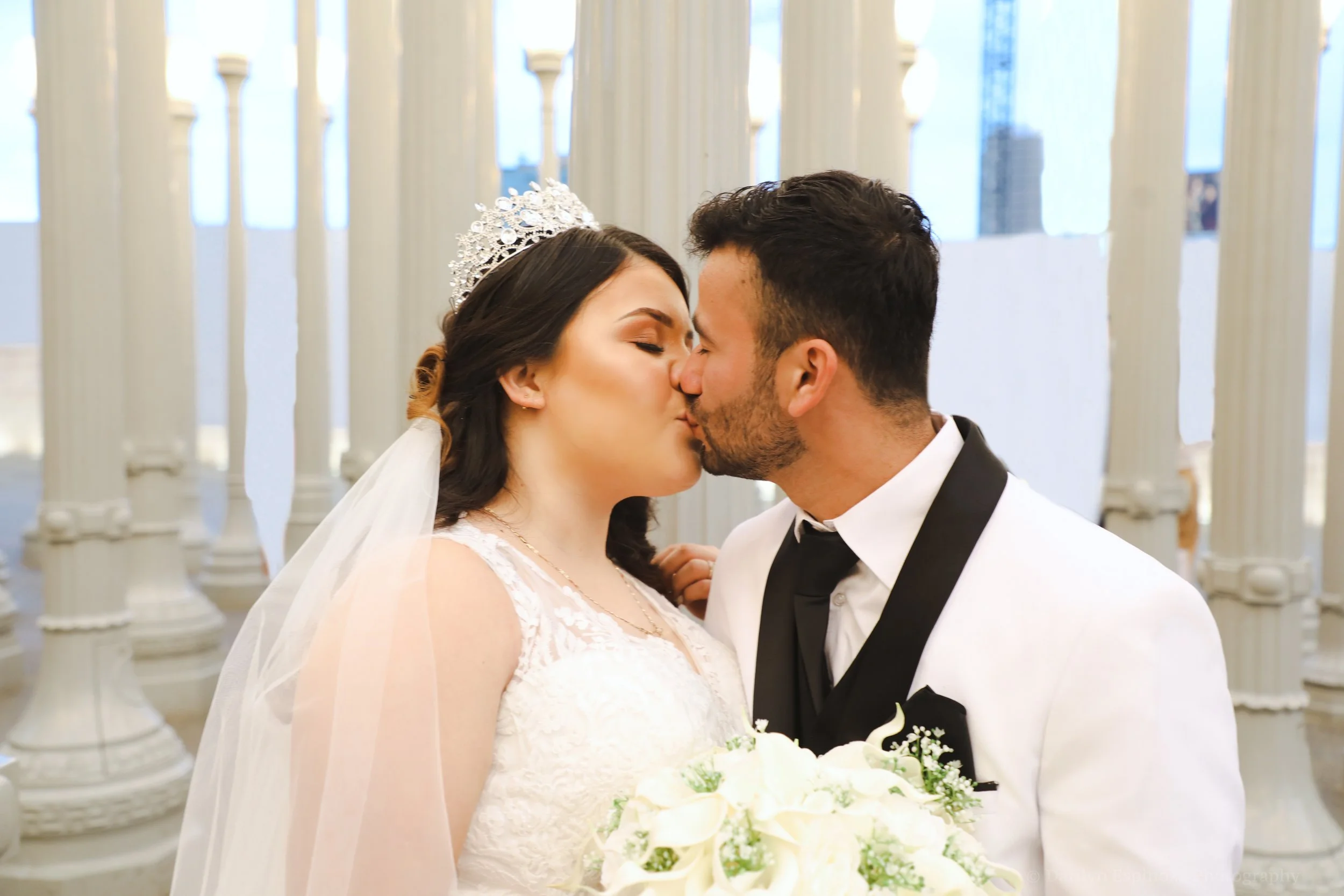 A bride and groom sharing a kiss in a wedding venue with white columns.