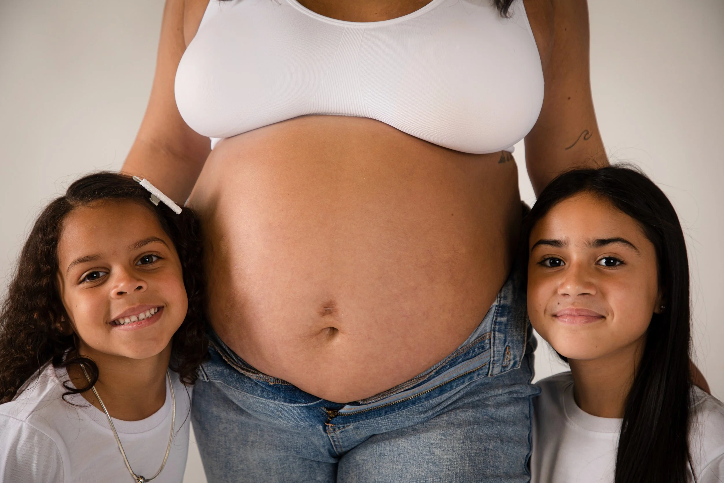An expectant woman with a pregnant belly standing between two young girls, all smiling at the camera.