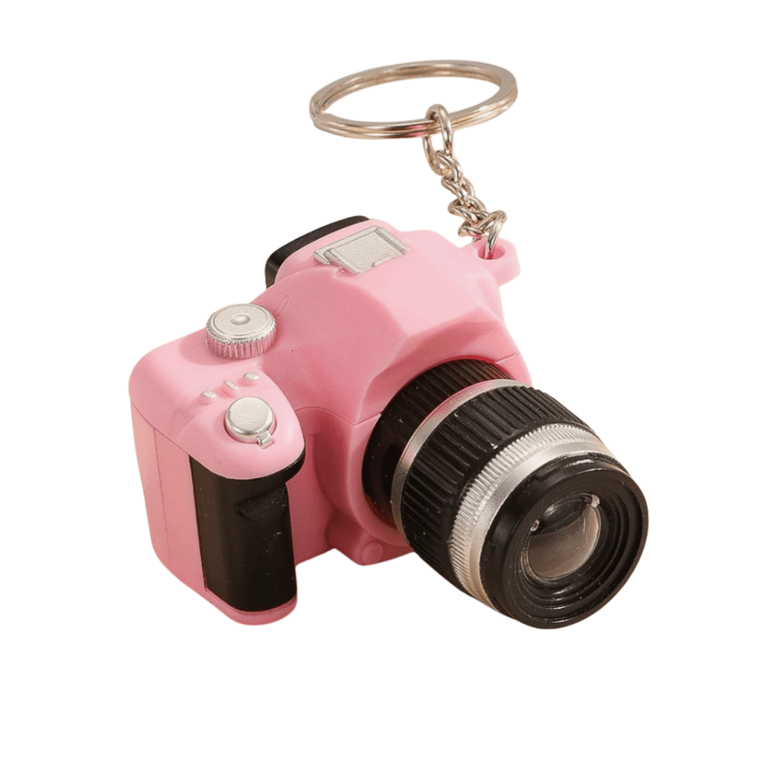 Pink camera-shaped keychain with a camera lens and a metal ring for attaching to keys.