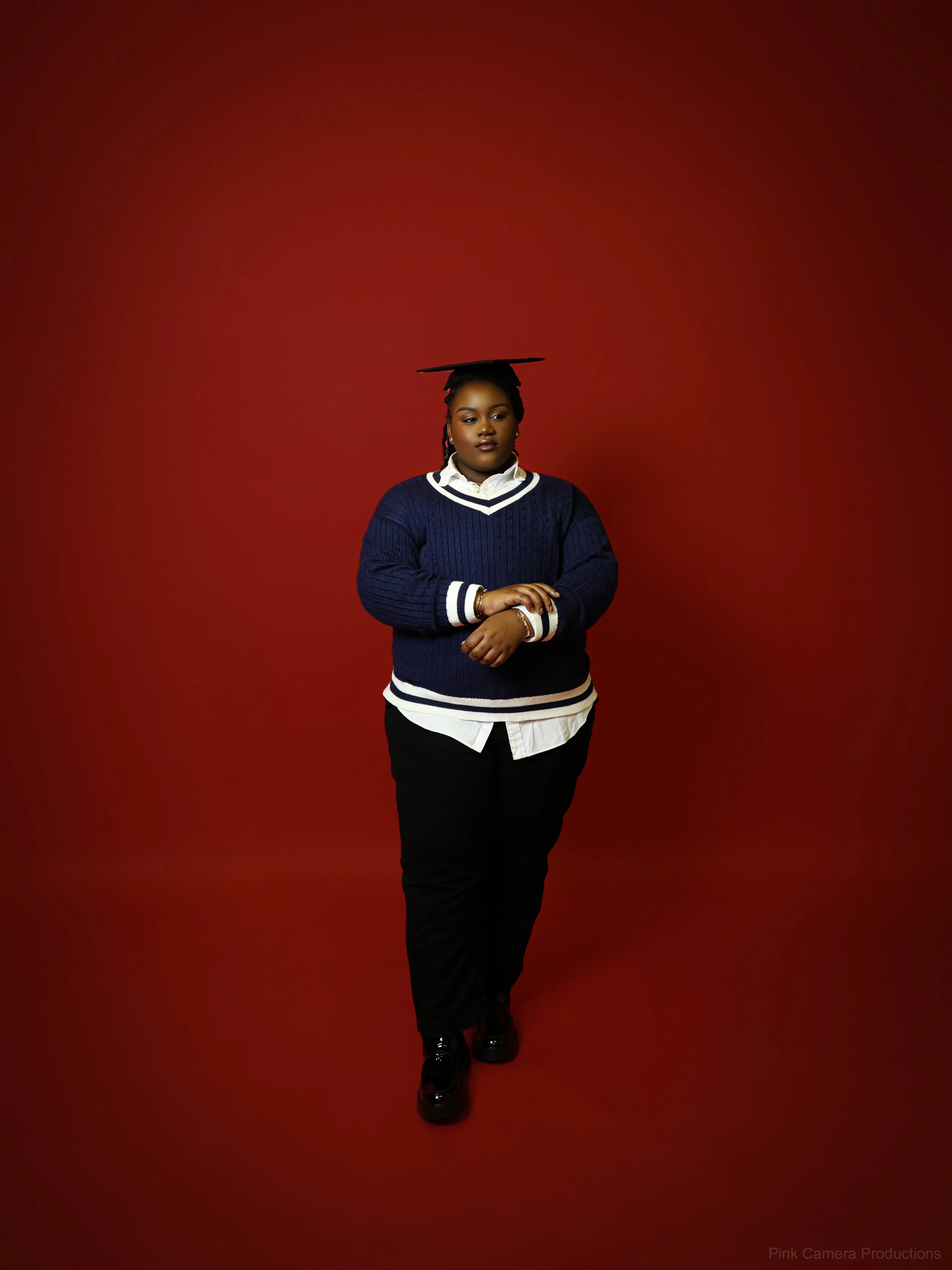 A woman in graduation cap and casual attire stands against a red background.