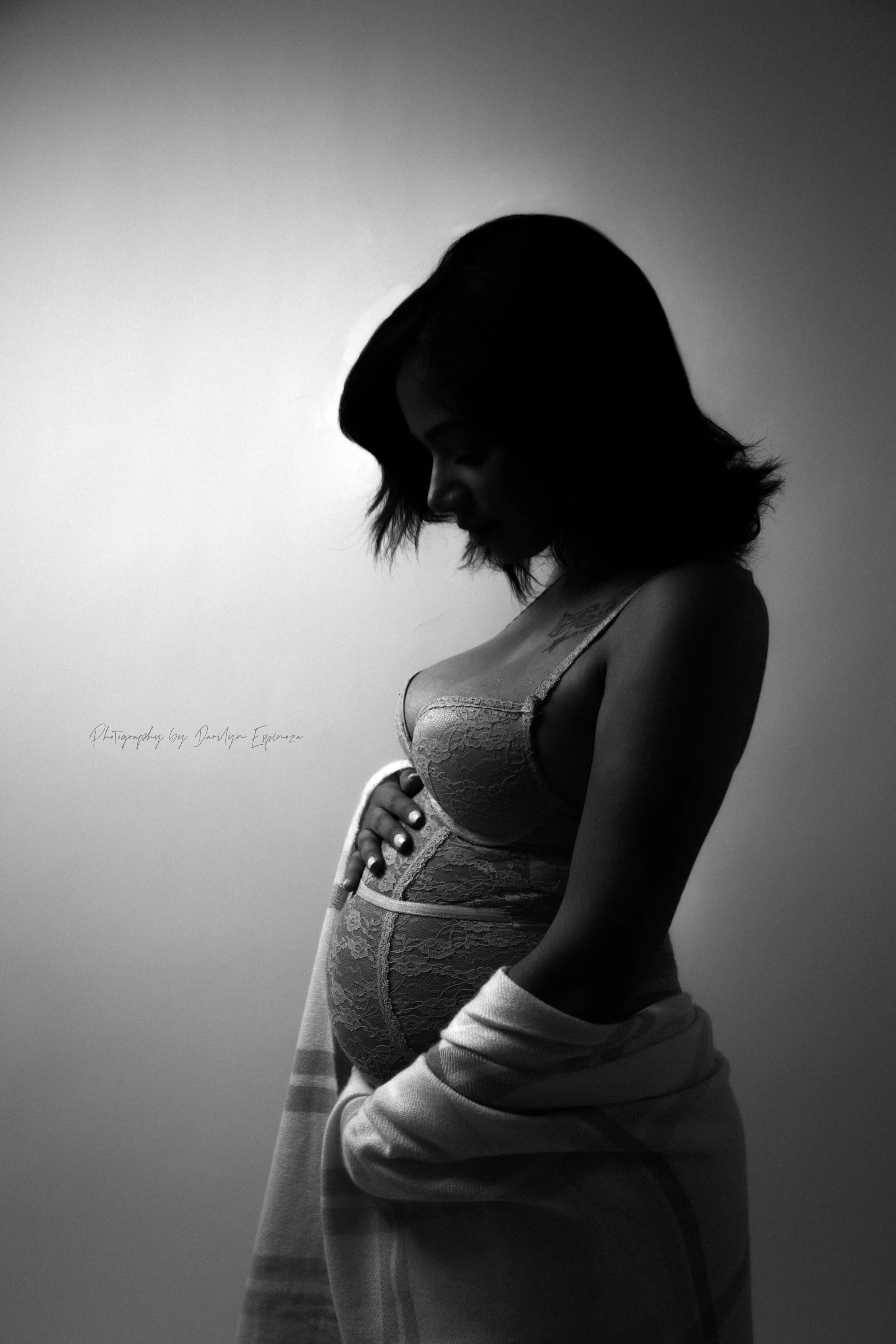 Black and white photo of a woman in lace lingerie, wrapped in a towel, looking down with her eyes closed, against a plain light background.