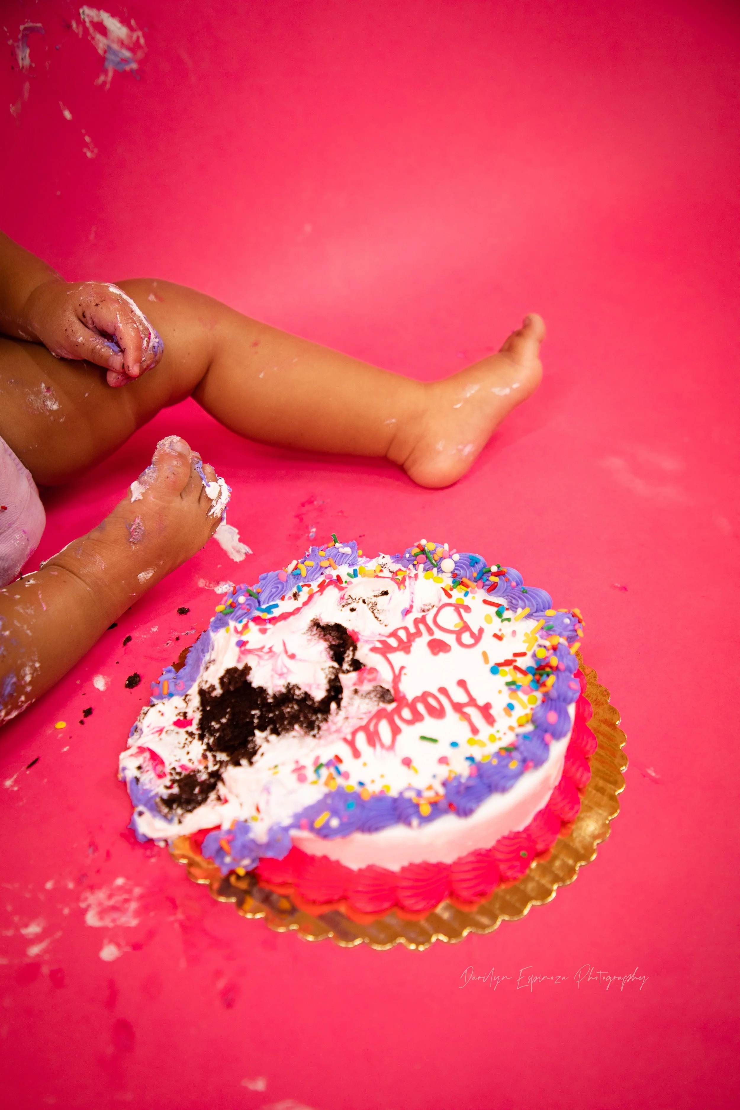 A messy birthday scene features wafer-covered children and a half-eaten birthday cake on a pink surface, with cake remnants, sprinkles, and frosting scattered around.