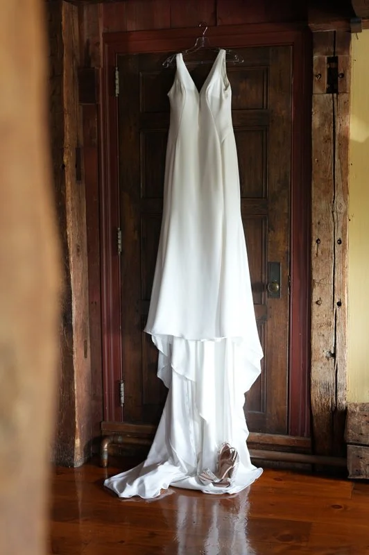 A white wedding dress hanging on a hanger in front of a wooden door.