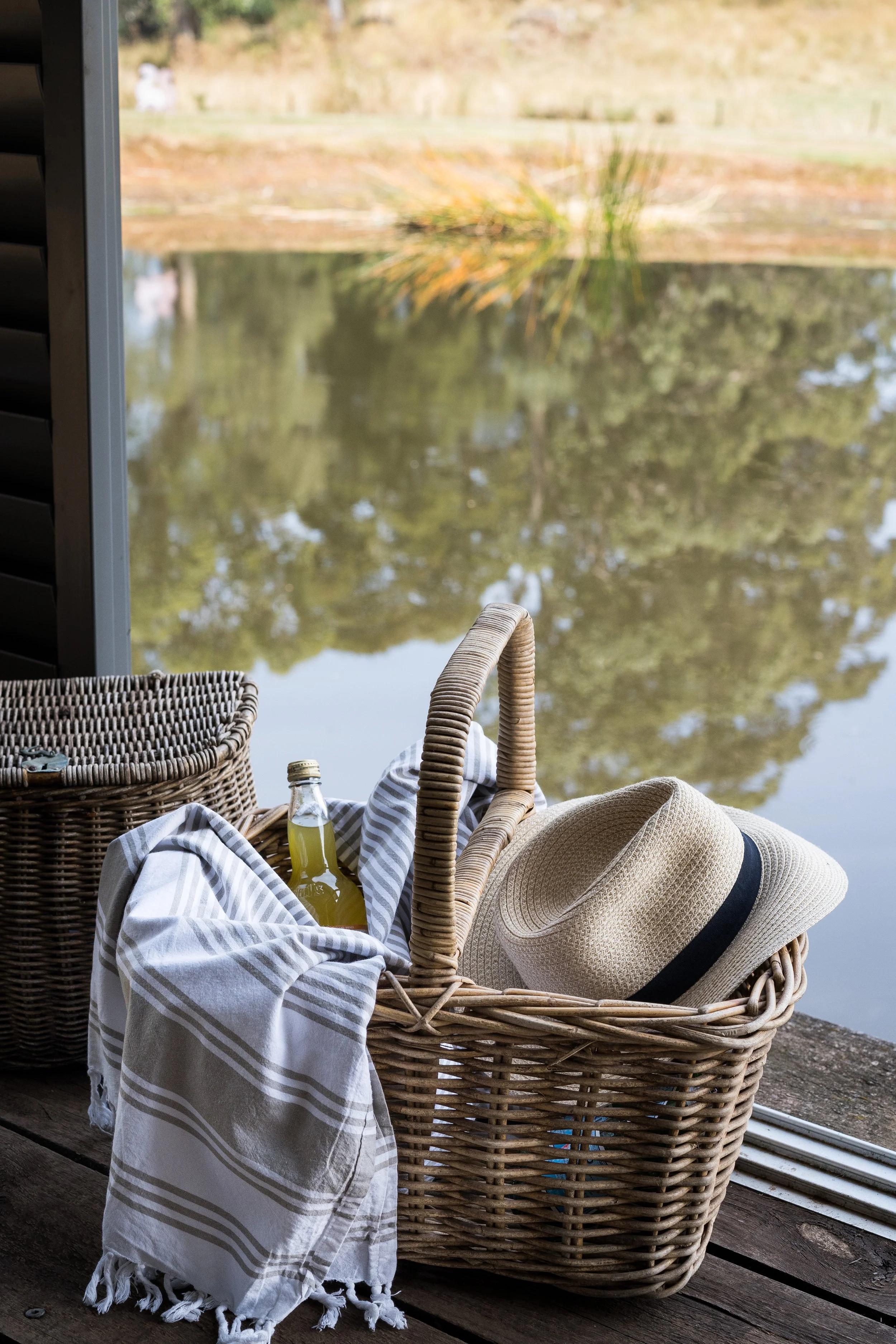 Styled holiday home deck with a picnic basket, striped throw and straw hat overlooking the water