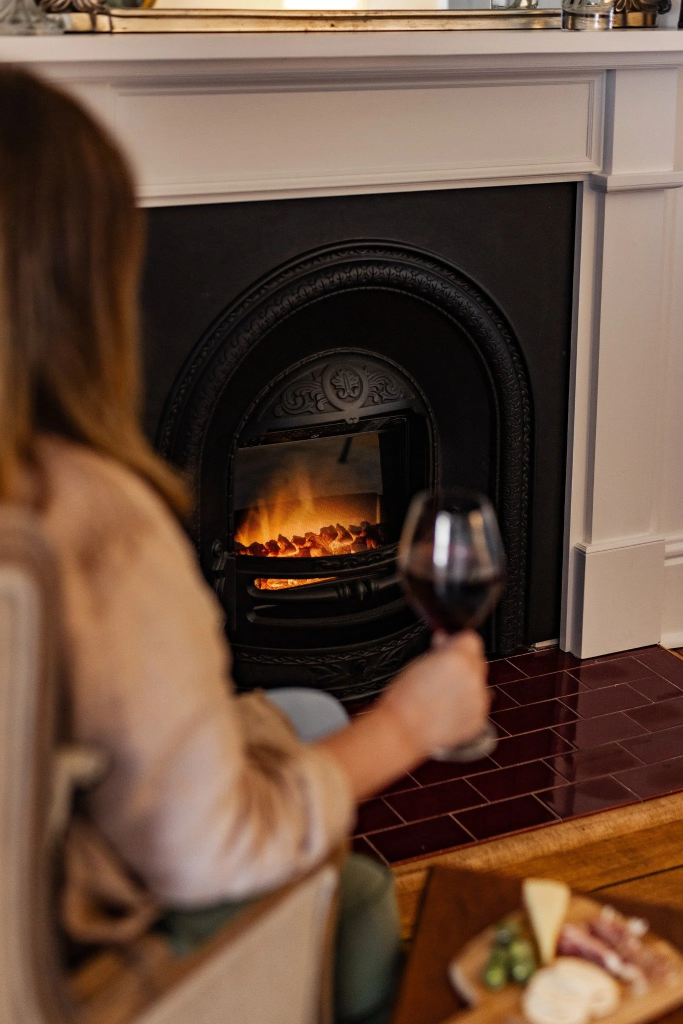 Guest relaxing with a glass of red wine beside a lit fireplace in a cosy holiday home