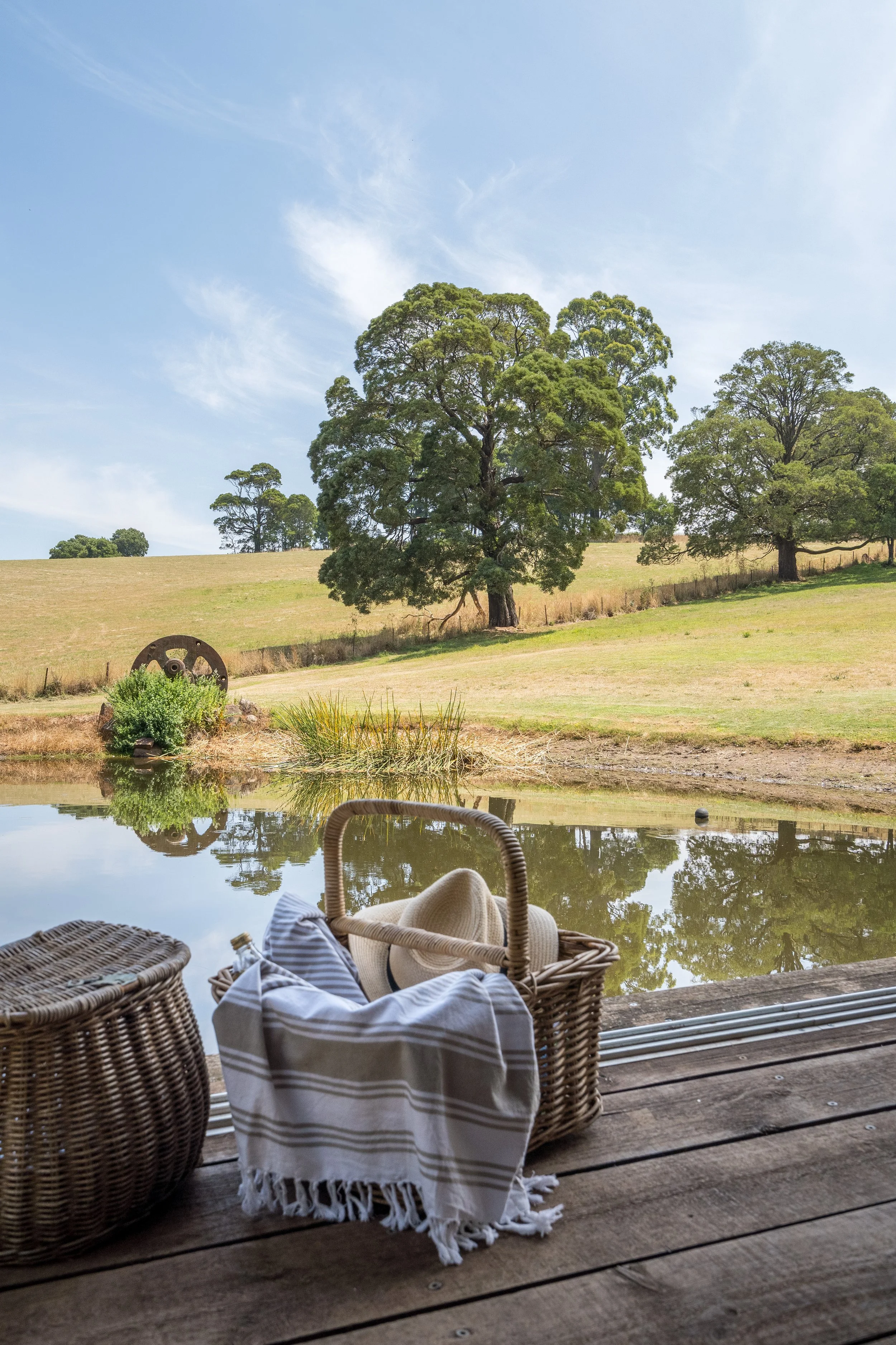 Picnic basket and checked throw on a timber jetty overlooking a dam and rolling countryside