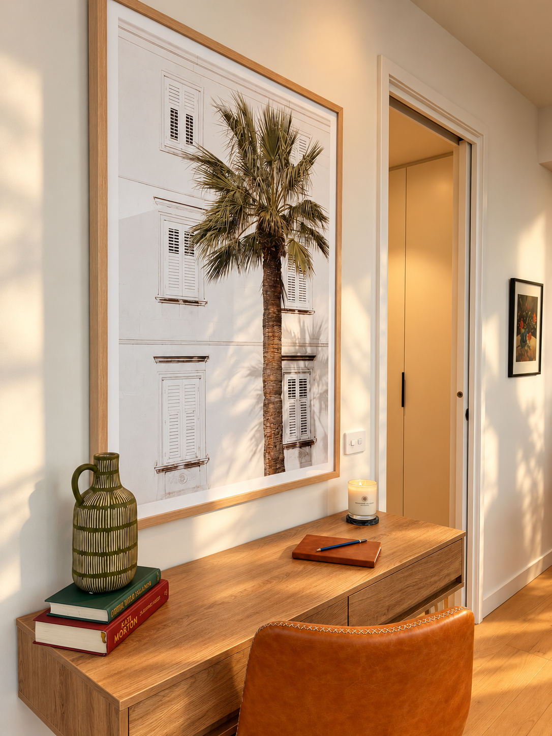 Styled Airbnb hallway with a large palm print artwork above a timber console, vase and books