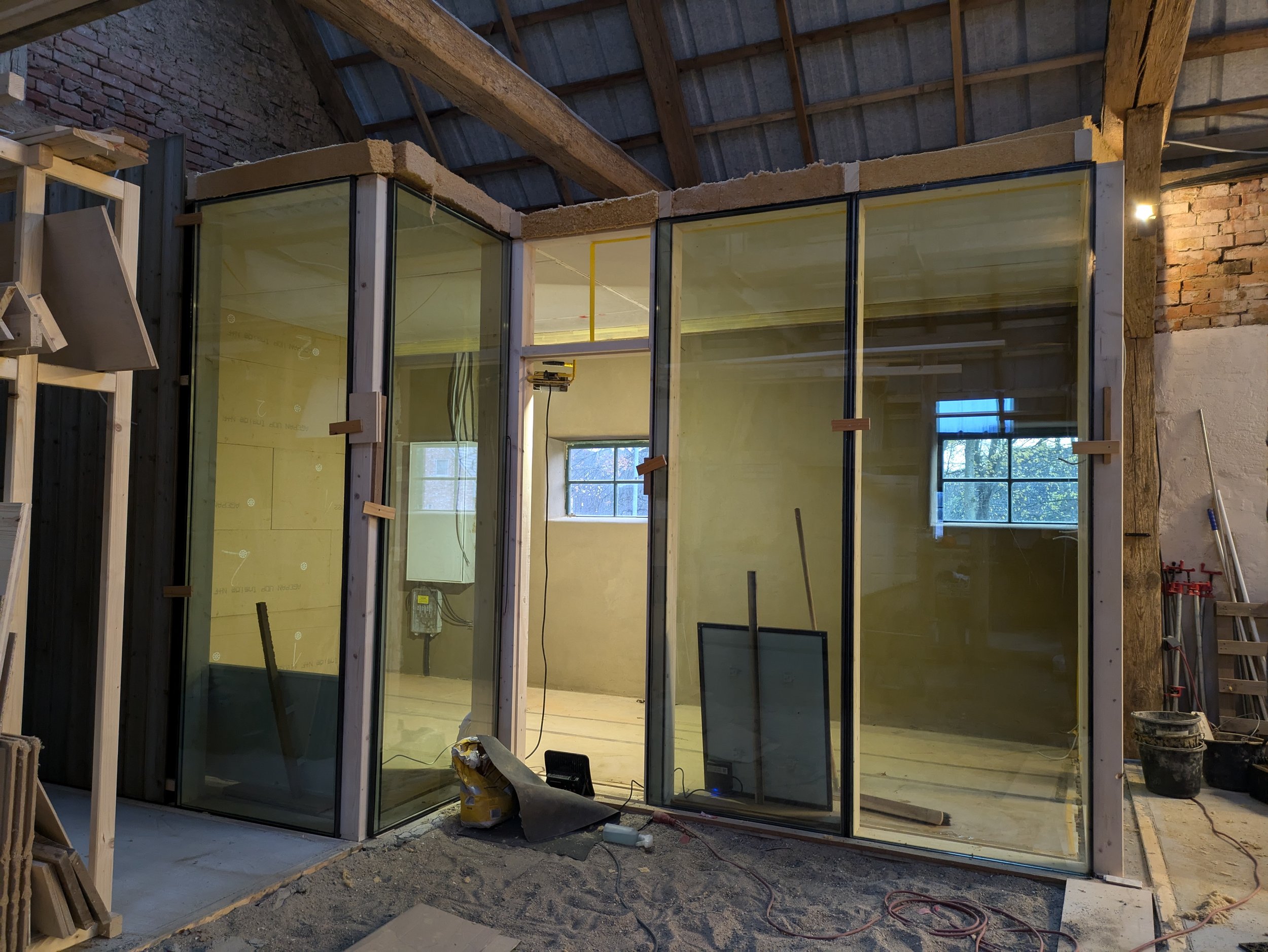Bau eines neuen Raumes mit Glaswänden in einem Innenraum, Bauwerkzeuge und Materialien sind sichtbar.