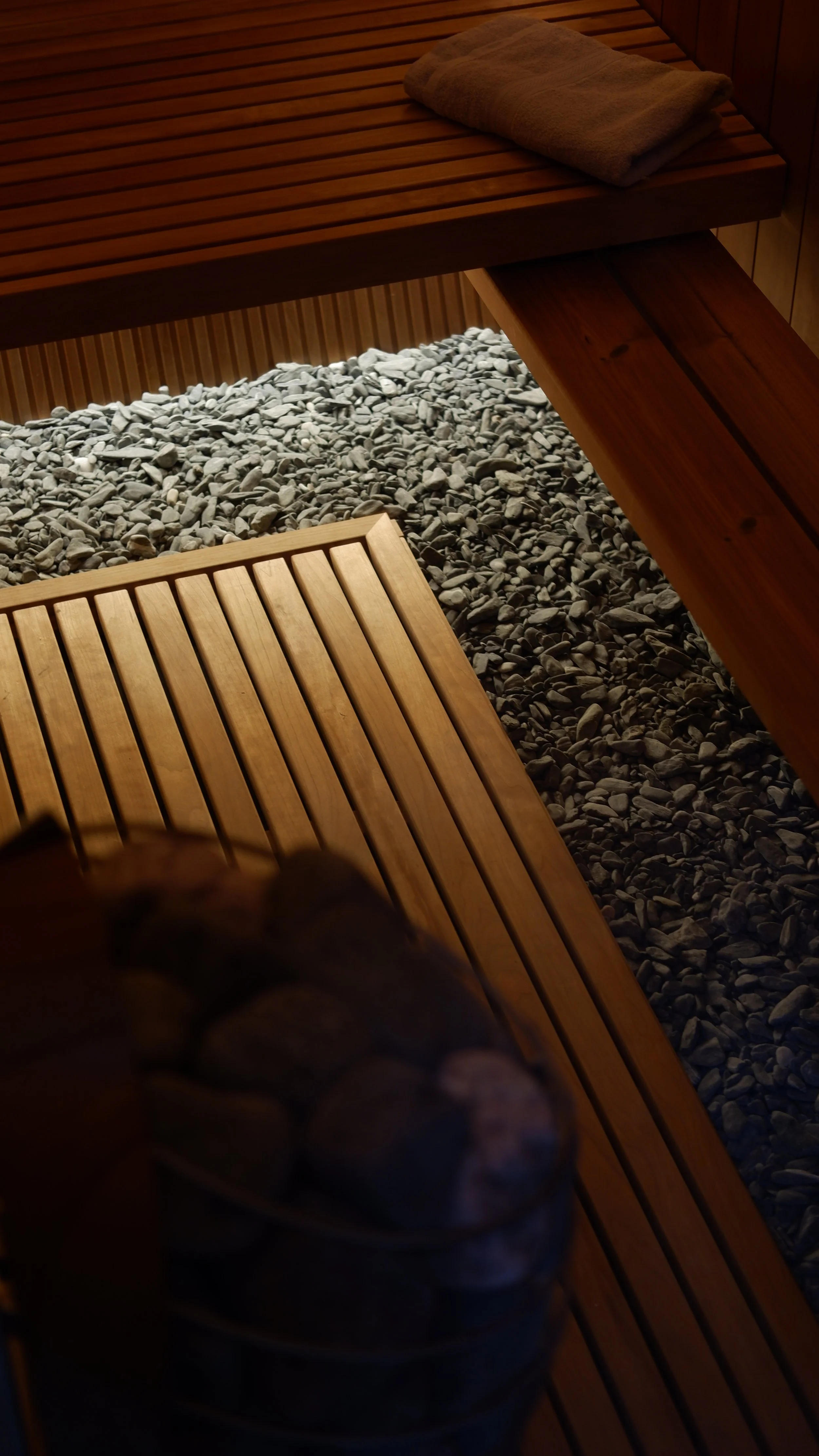 Holzbank und Handtücher in einer Sauna, Steine auf dem Boden.