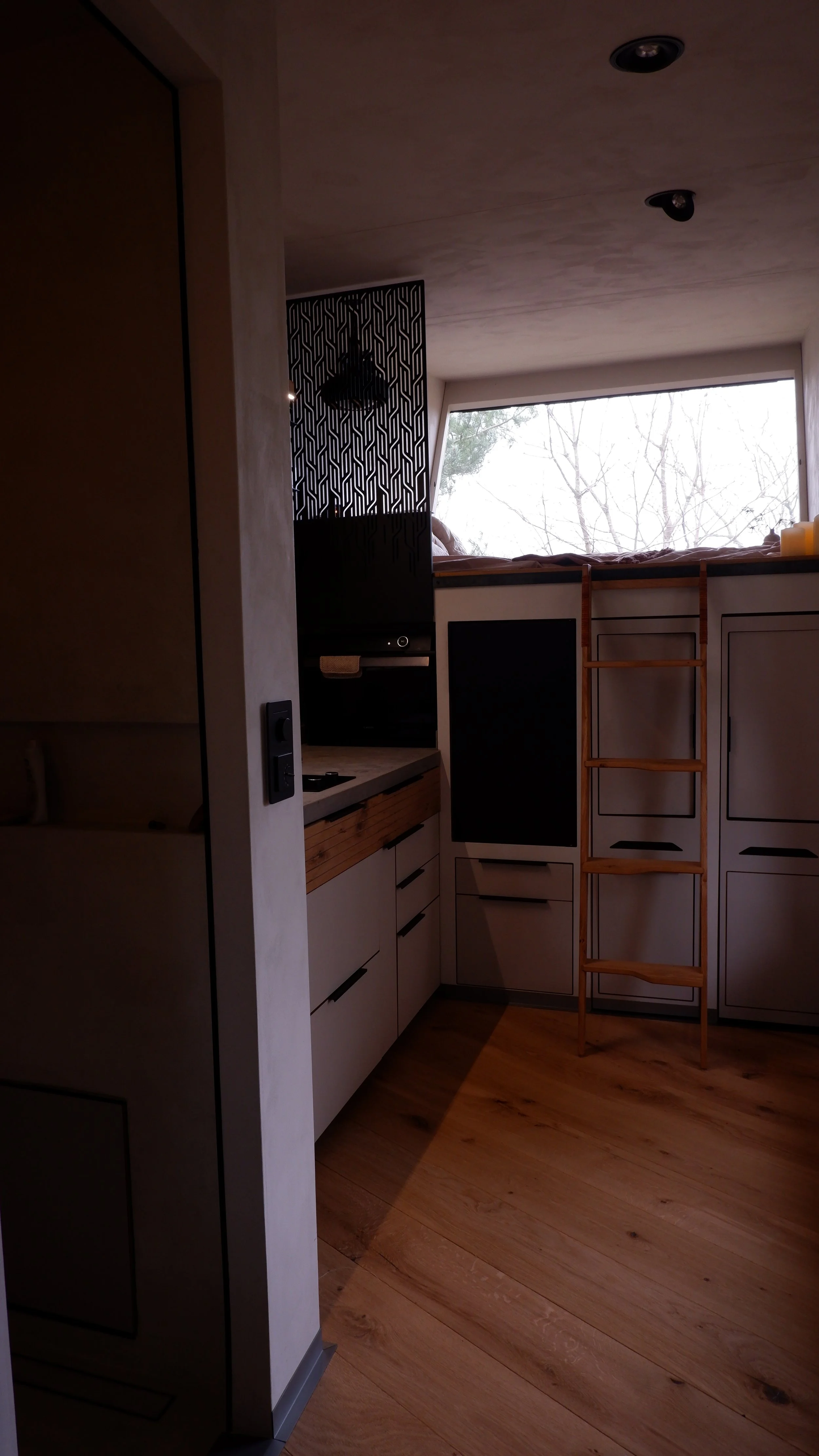 Innenaufnahme einer modernen Küche mit Wardrobe, Holztreppe, großen Fenster und Sicht auf Winterbäume im Hintergrund.