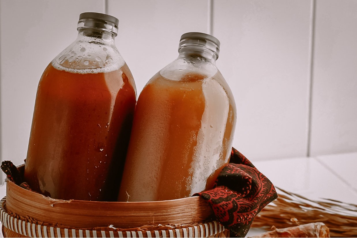 Two glass bottles filled with brown liquid and sealed with black caps, placed in a woven basket.