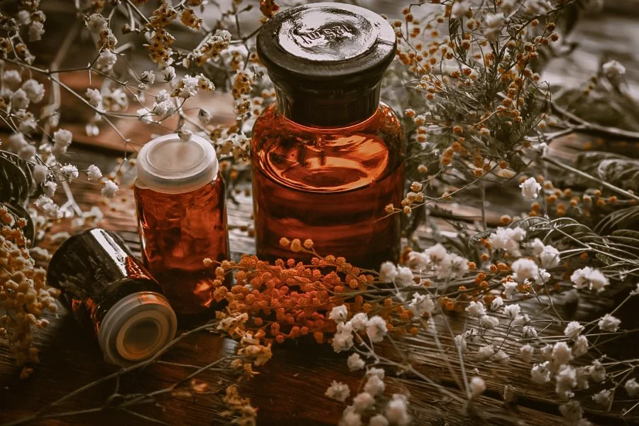 Vintage amber glass bottles surrounded by dried flowers on a wooden surface.