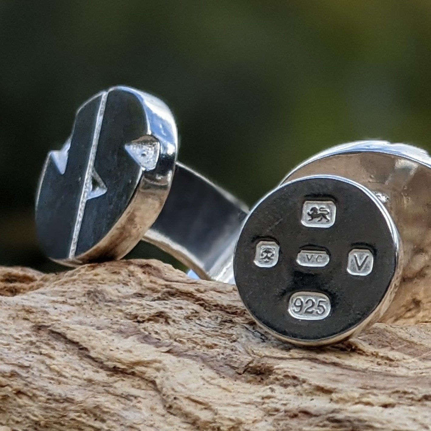 Close-up of silver cufflinks with engraved hallmark symbols, including '925'.