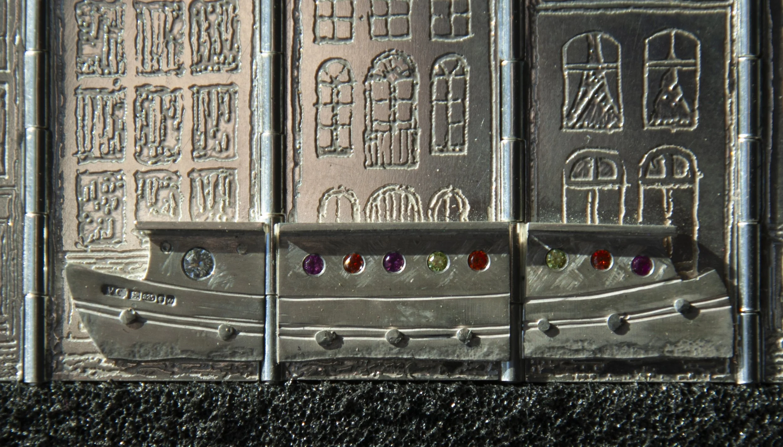 Metal sculpture depicting buildings and a boat with colored gems