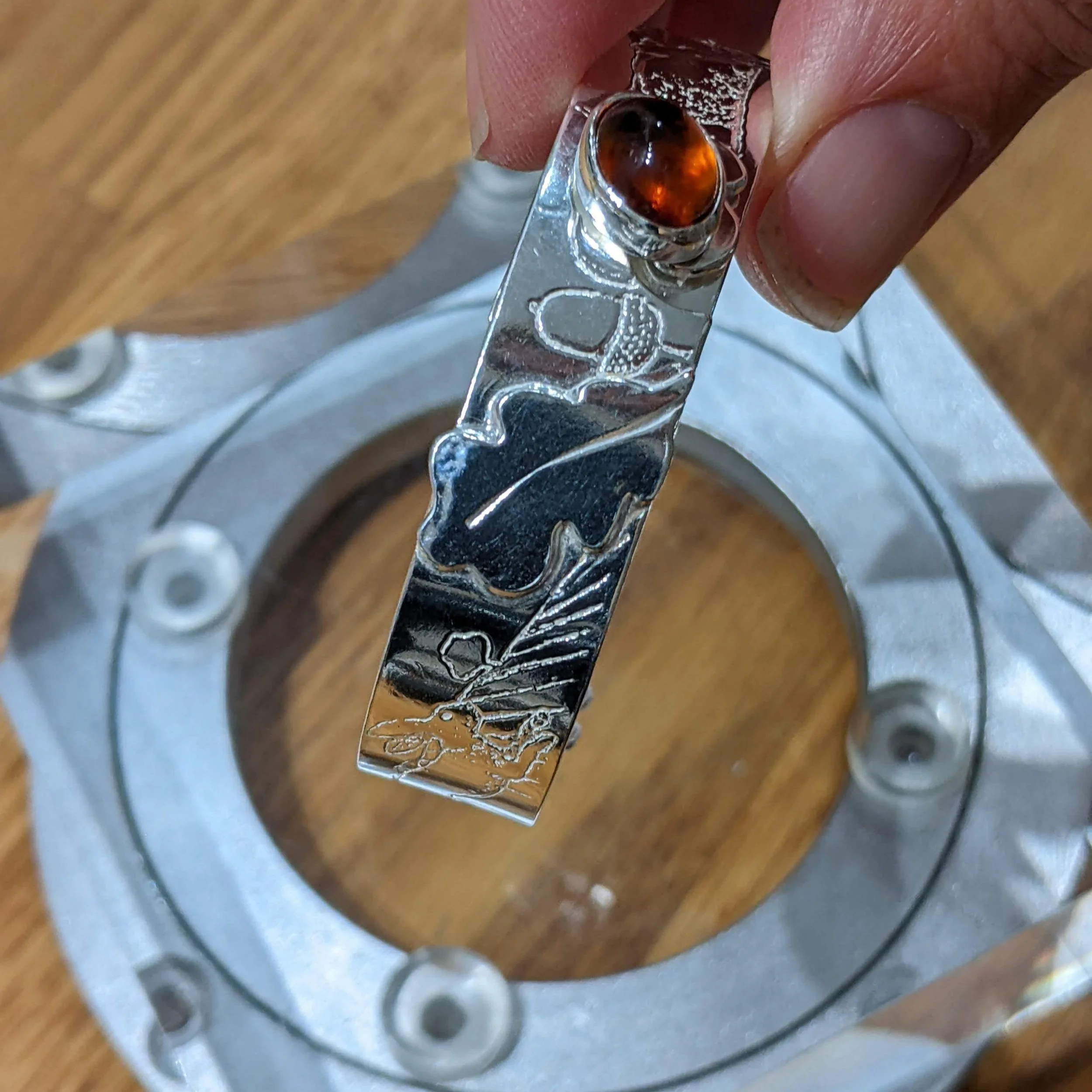 A close-up of a person holding a silver bracelet with intricate engravings, featuring a madiera citrine gemstone.