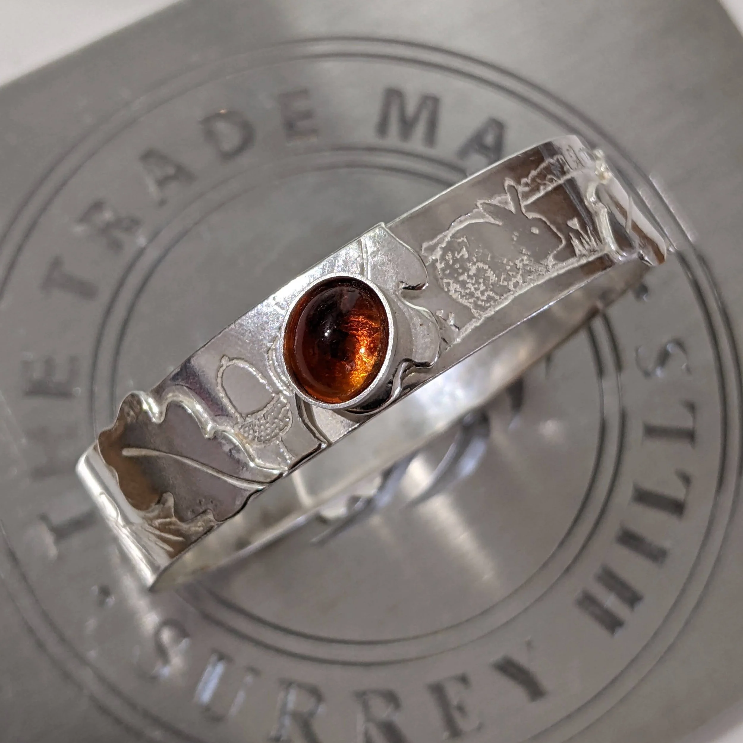 Silver bracelet with madiera citrine gemstone and engraved animal design on a metal background.