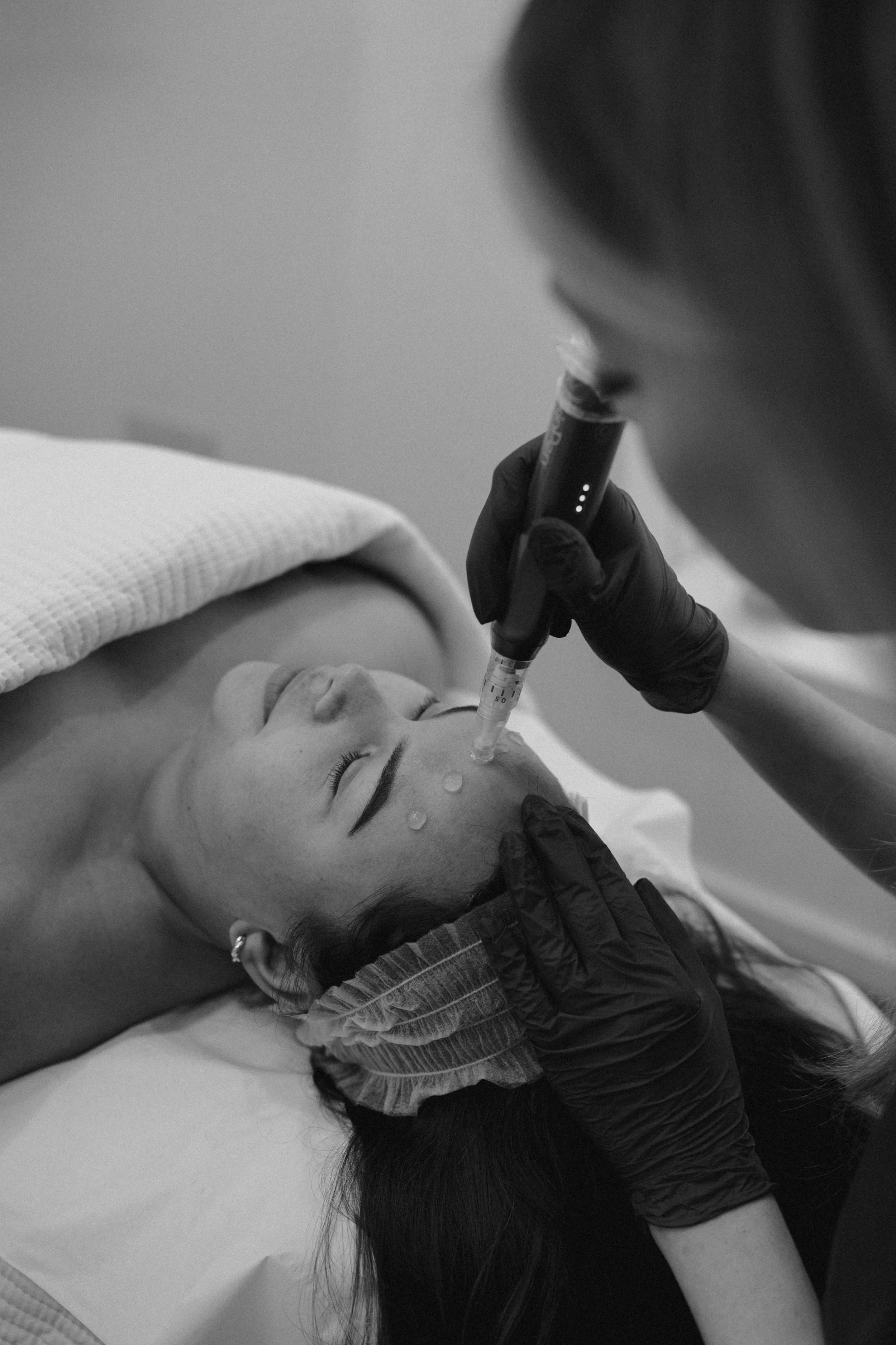 A woman receiving a cosmetic injection on her forehead in a clinical setting.