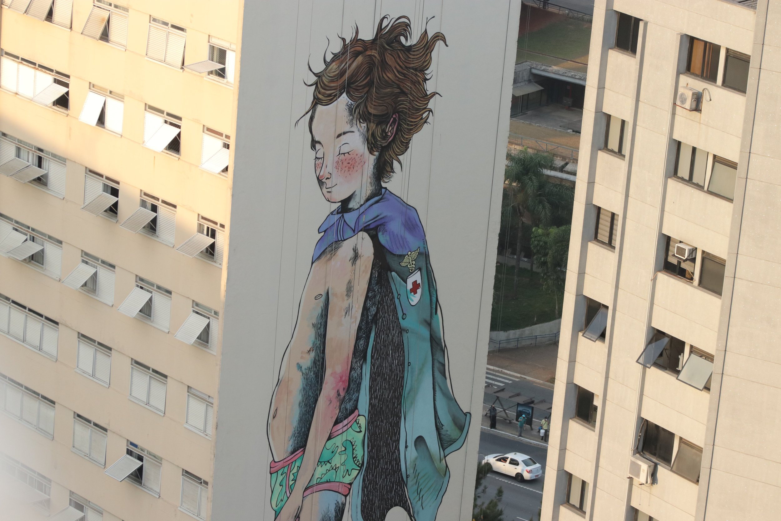 Mural de um garoto em um prédio, com cabelo solto ao vento e olhos fechados.