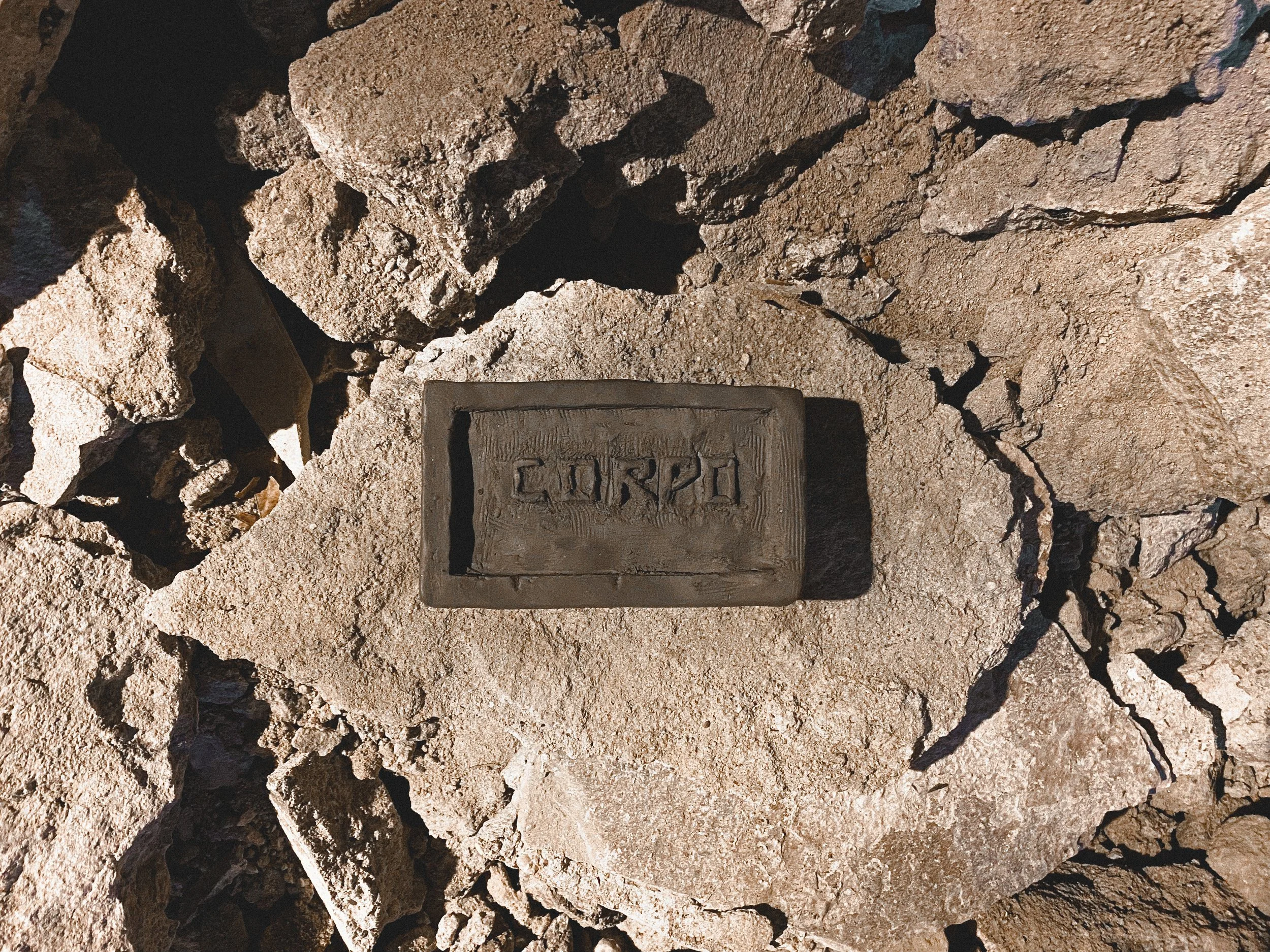 Pedra com inscrição em português, rodeada de pedras soltas.