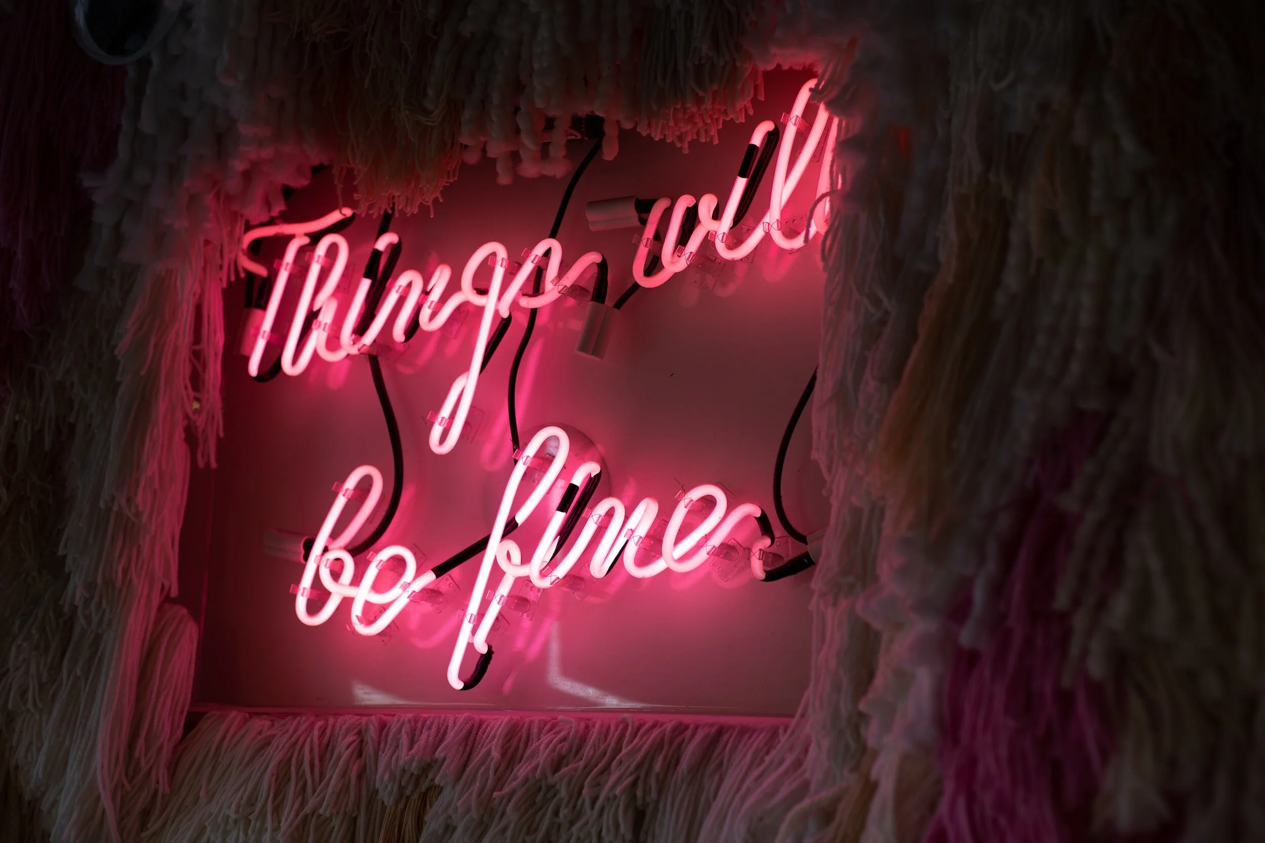 Pink neon sign that reads "Through to be Love" surrounded by fluffy textured materials.