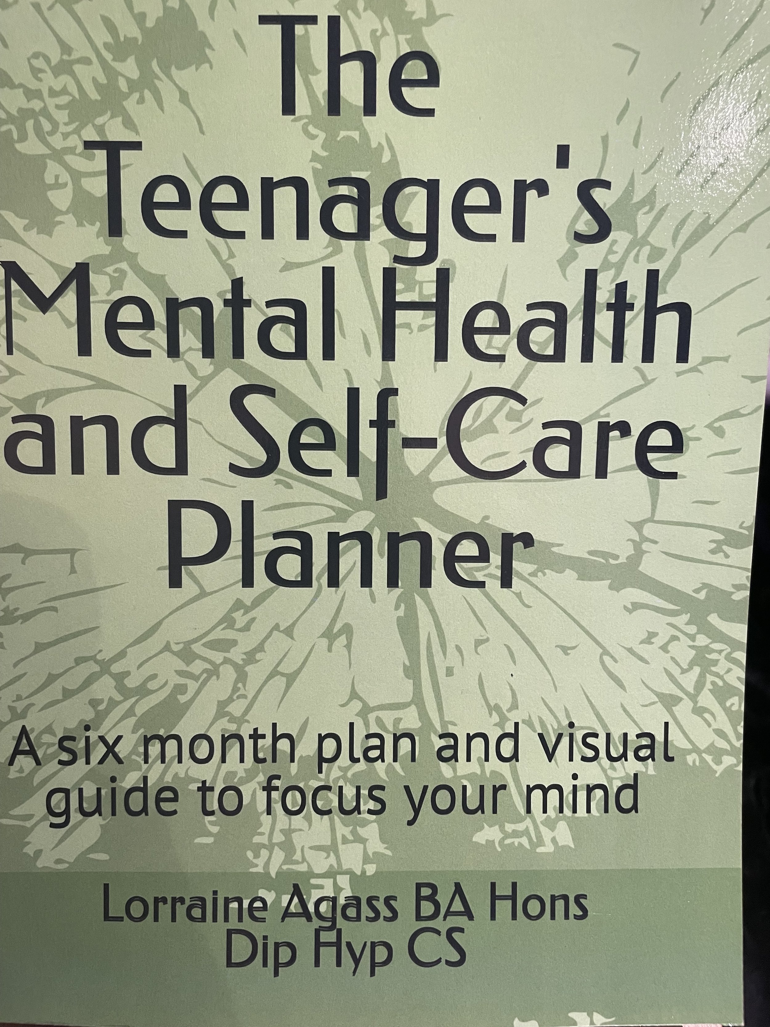 Cover of a planner titled 'The Teenager's Mental Health and Self-Care Planner,' with a light green background and an illustration of a tree on it. Subtitle reads 'A six month plan and visual guide to focus your mind.' Author is Lorraine Agass BA Hons Dip Hyp CS.