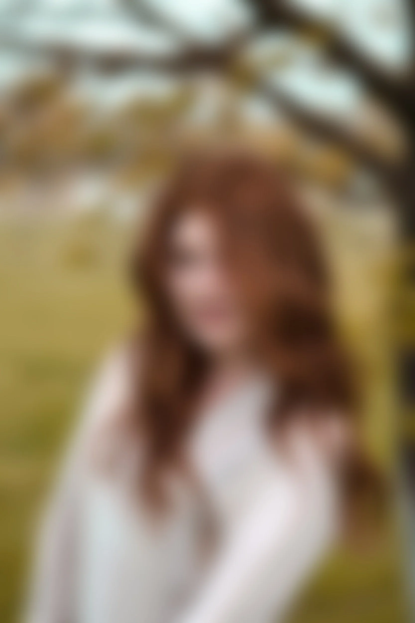 Blurred image of a person with long, brown hair, standing outdoors near trees.